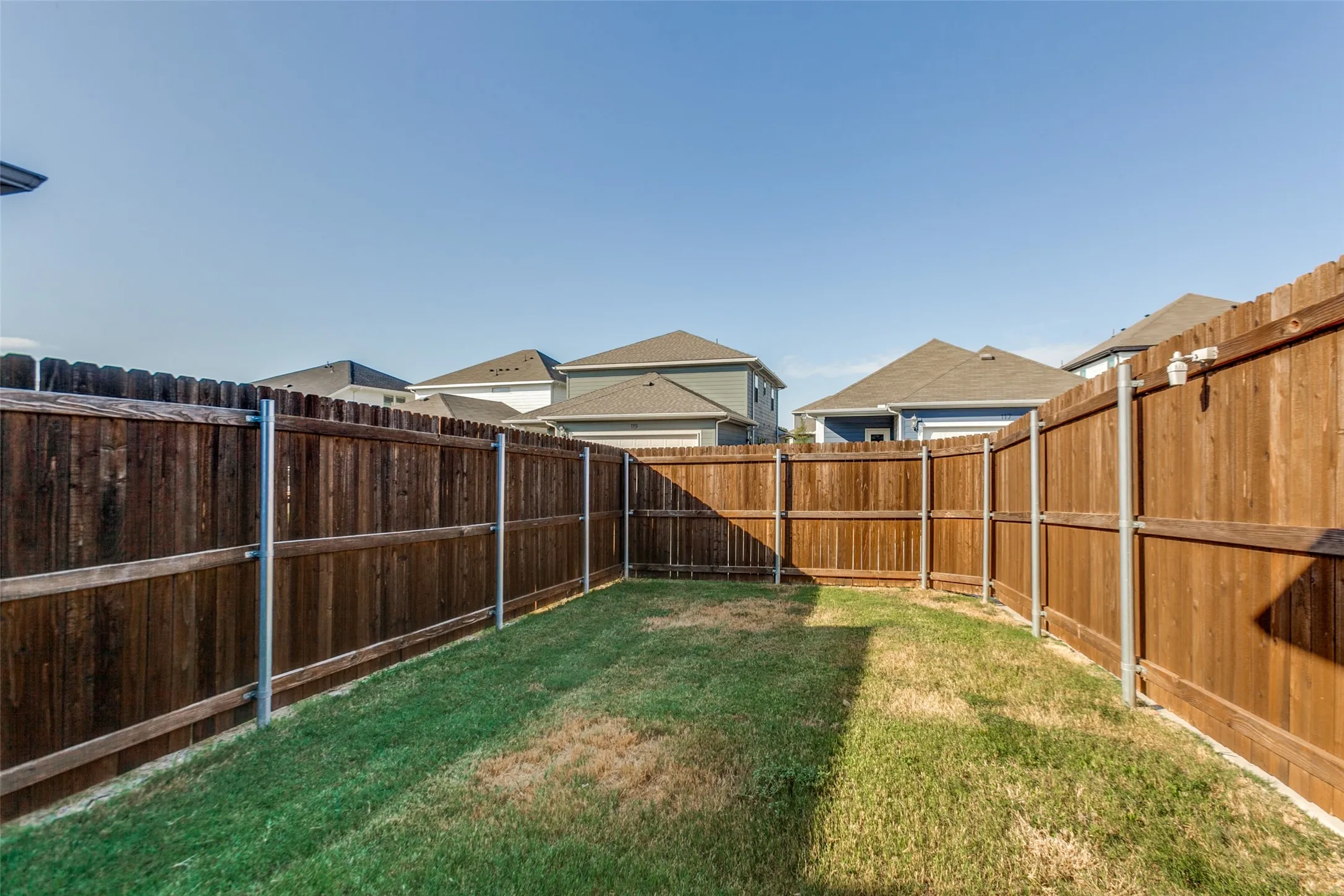 Fenced backyard featuring a wood privacy fence with metal posts and a grass lawn