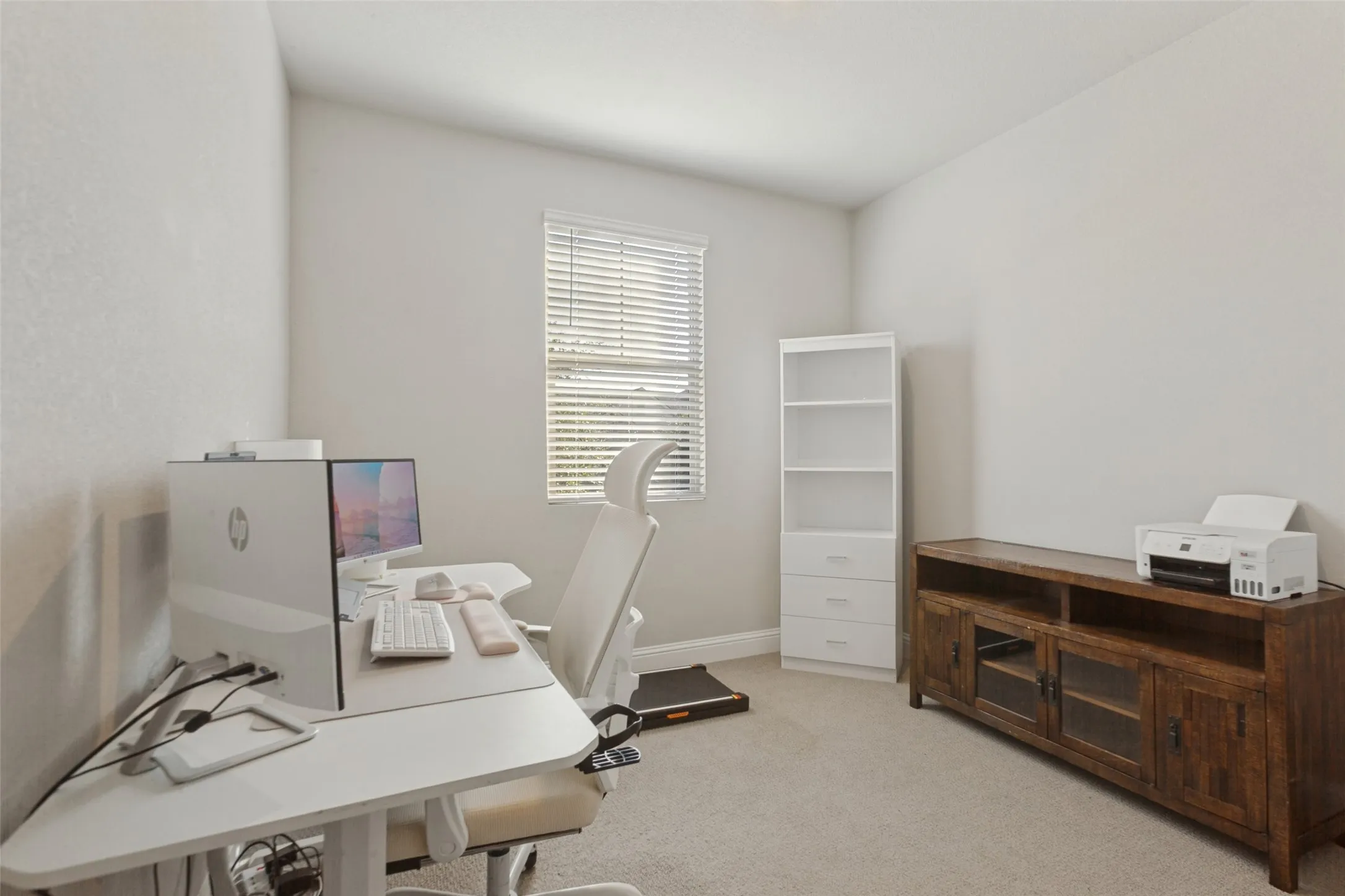 Neutral wall color, window with blinds, carpet flooring, built-in shelving, and a wood-finish media console