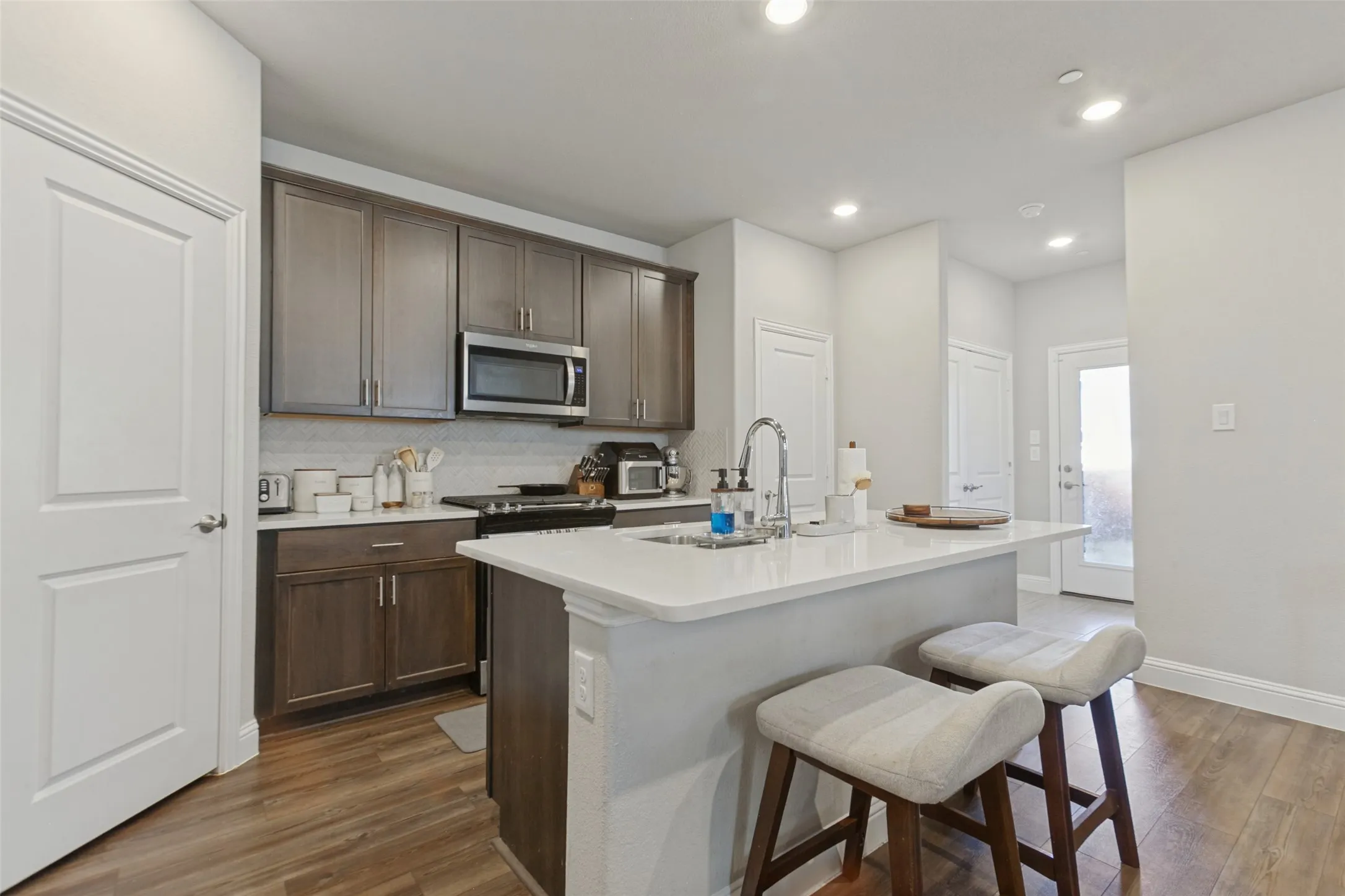 Kitchen featuring a central island, stainless steel microwave, dark wood-finish cabinetry, light-toned countertops, and wood-finish flooring