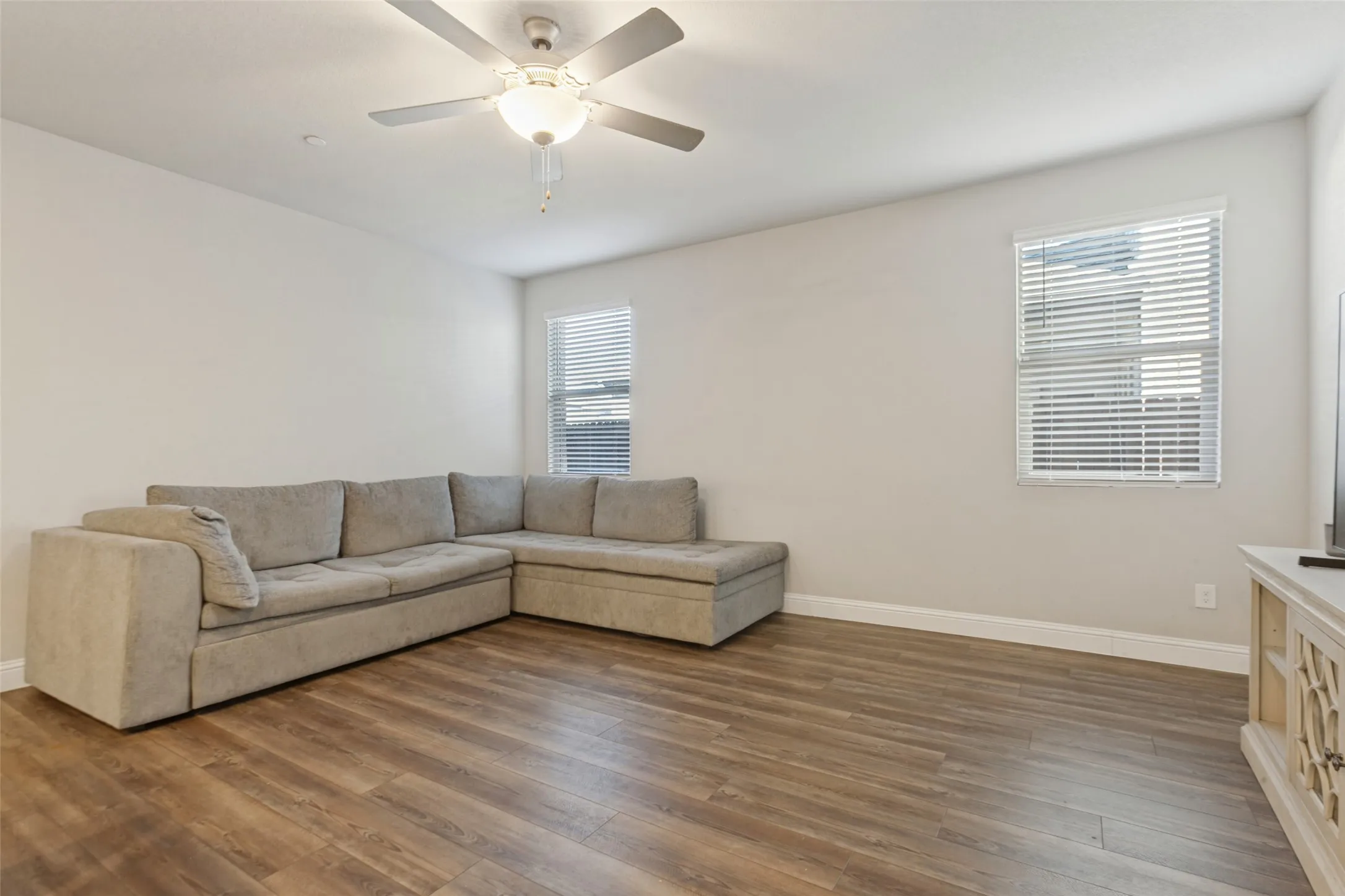 Spacious living room with neutral wall finishes, hard wood-finish flooring throughout, and abundant natural light from dual windows with plantation shutters