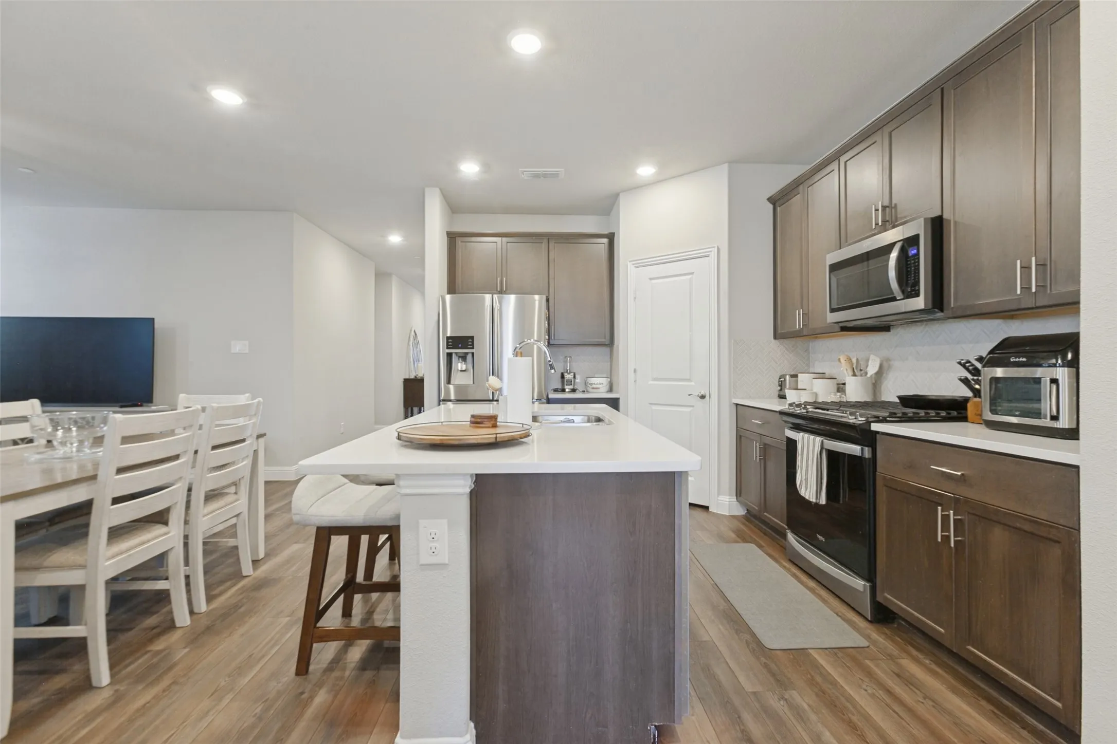 Kitchen featuring recessed lighting, a built-in microwave, stainless steel appliances, a white subway tile backsplash, and an expansive island with a white countertop