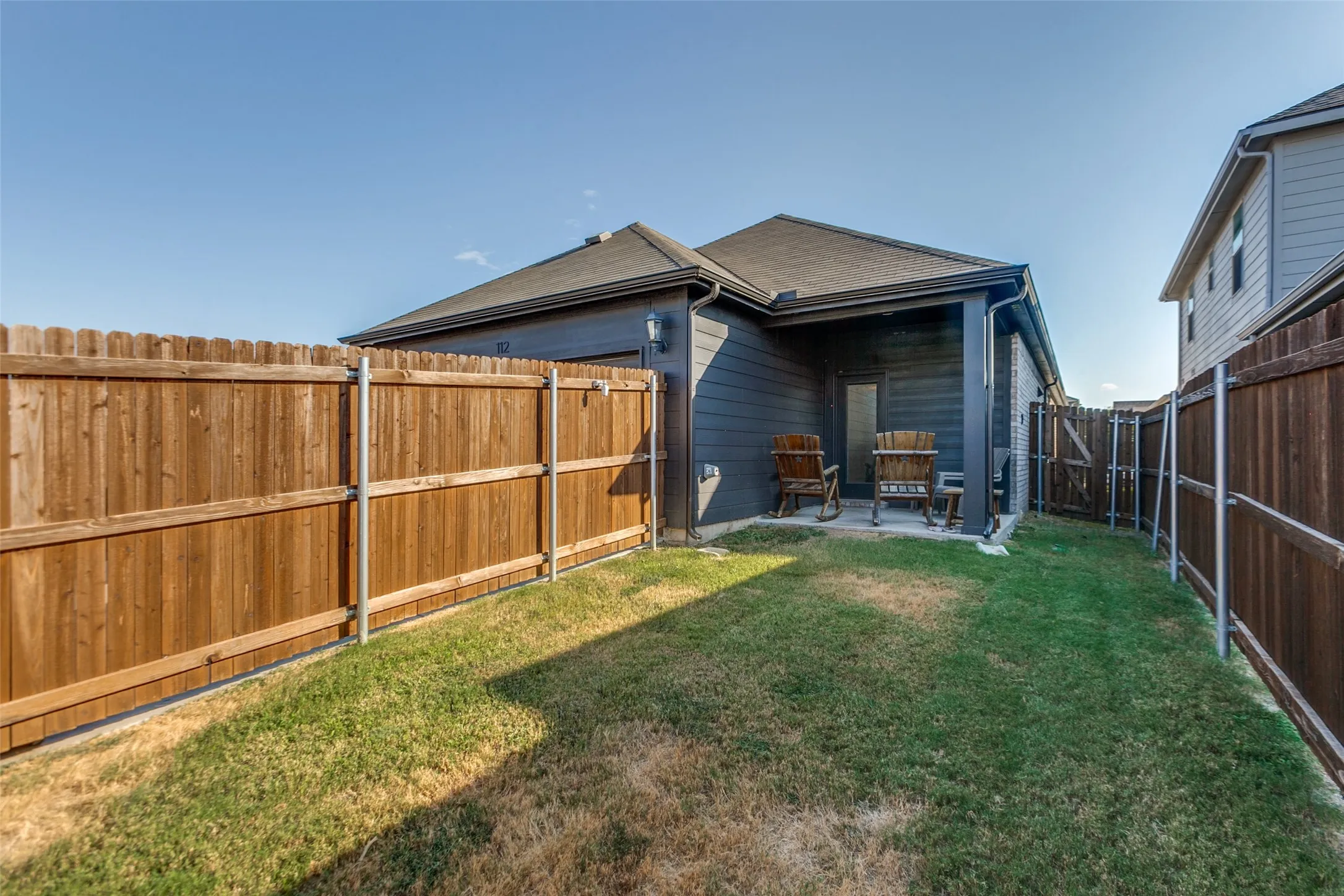 Spacious backyard with mature lawn, wood-finish privacy fencing, and covered patio extension
