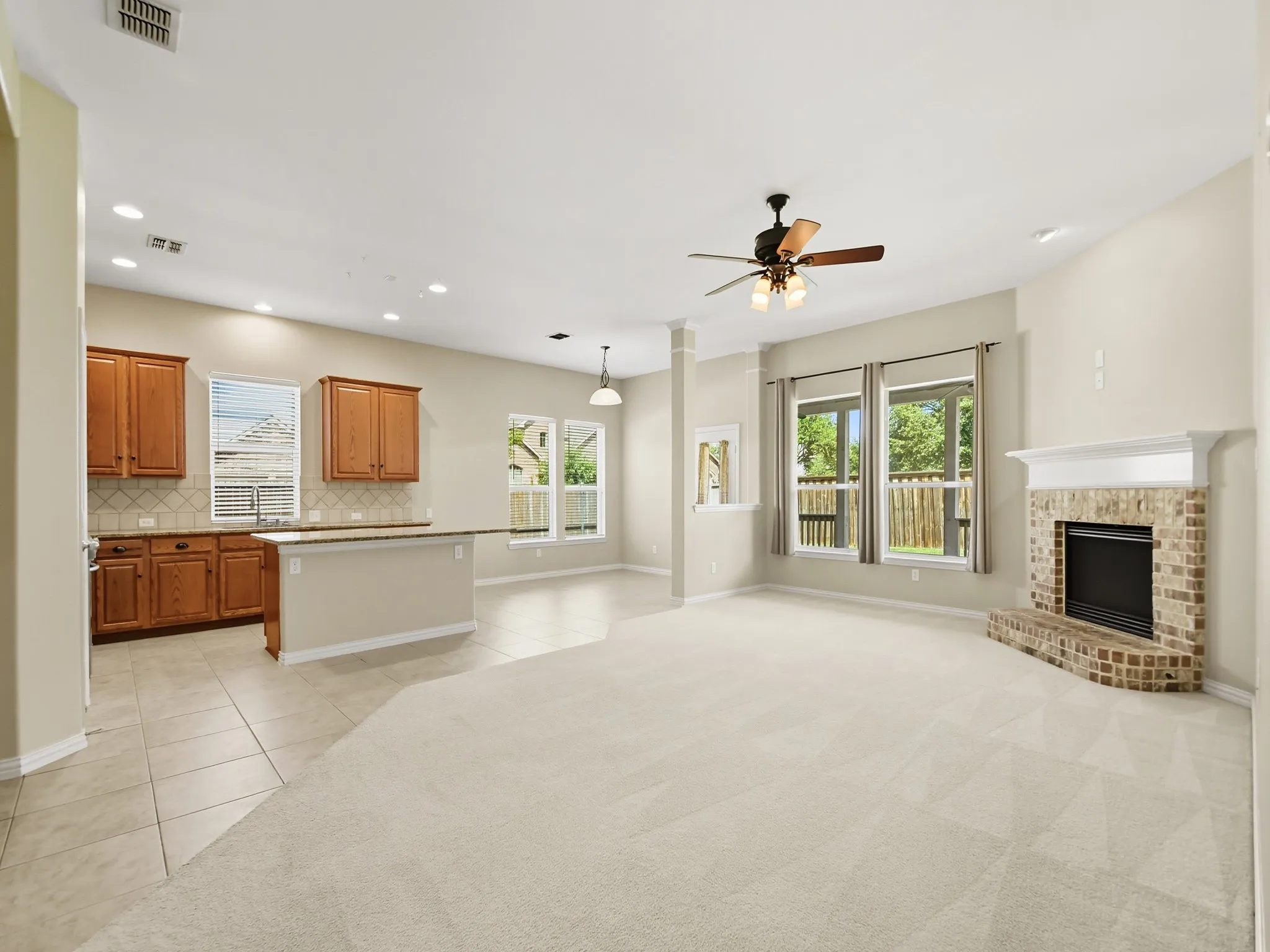 Open-concept living area featuring a brick fireplace with a white mantel, multiple windows, a ceiling fan, and recessed lighting
