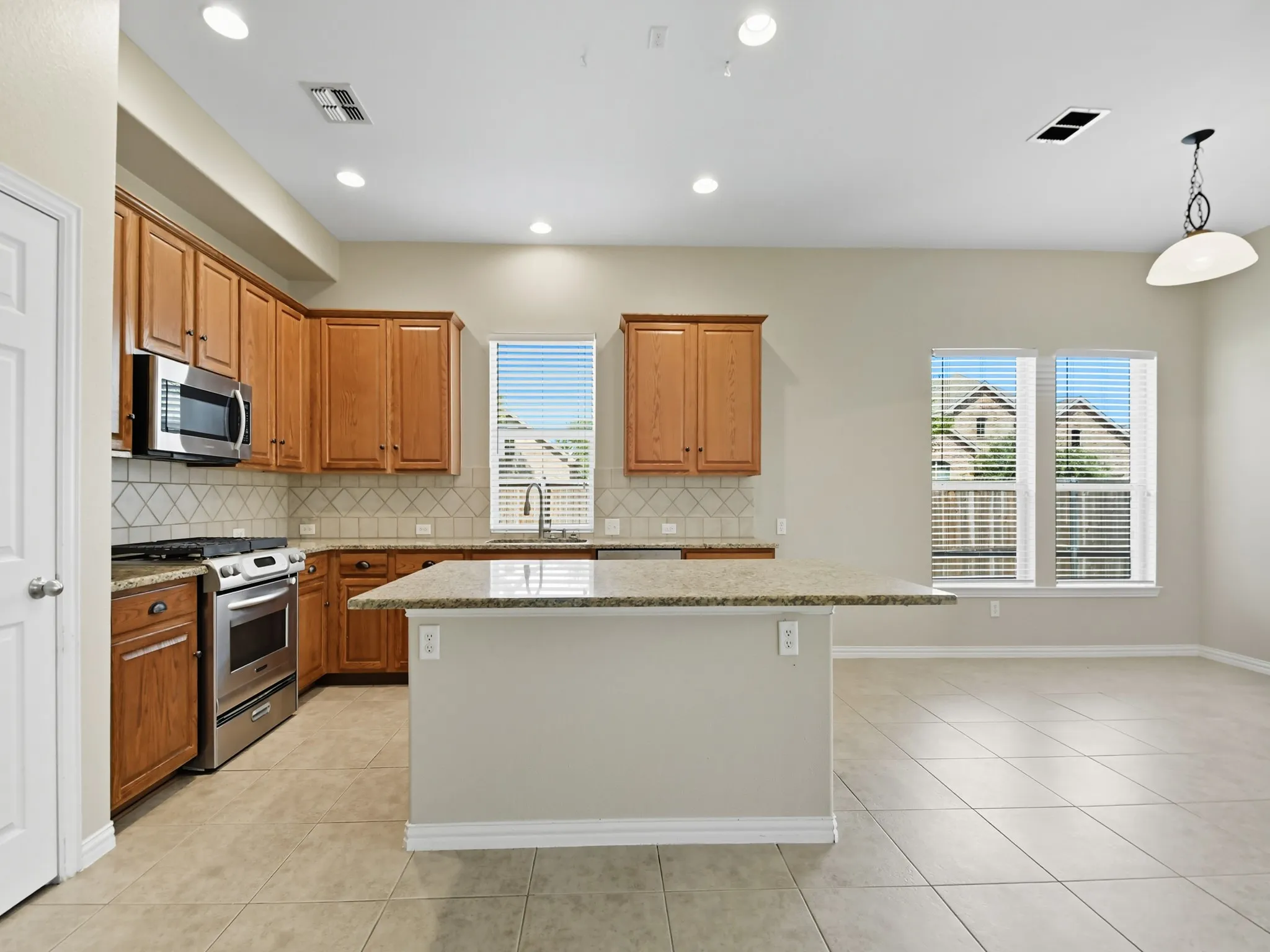 Kitchen featuring a center island, stainless steel appliances, wood cabinetry, tile flooring, and a tile backsplash