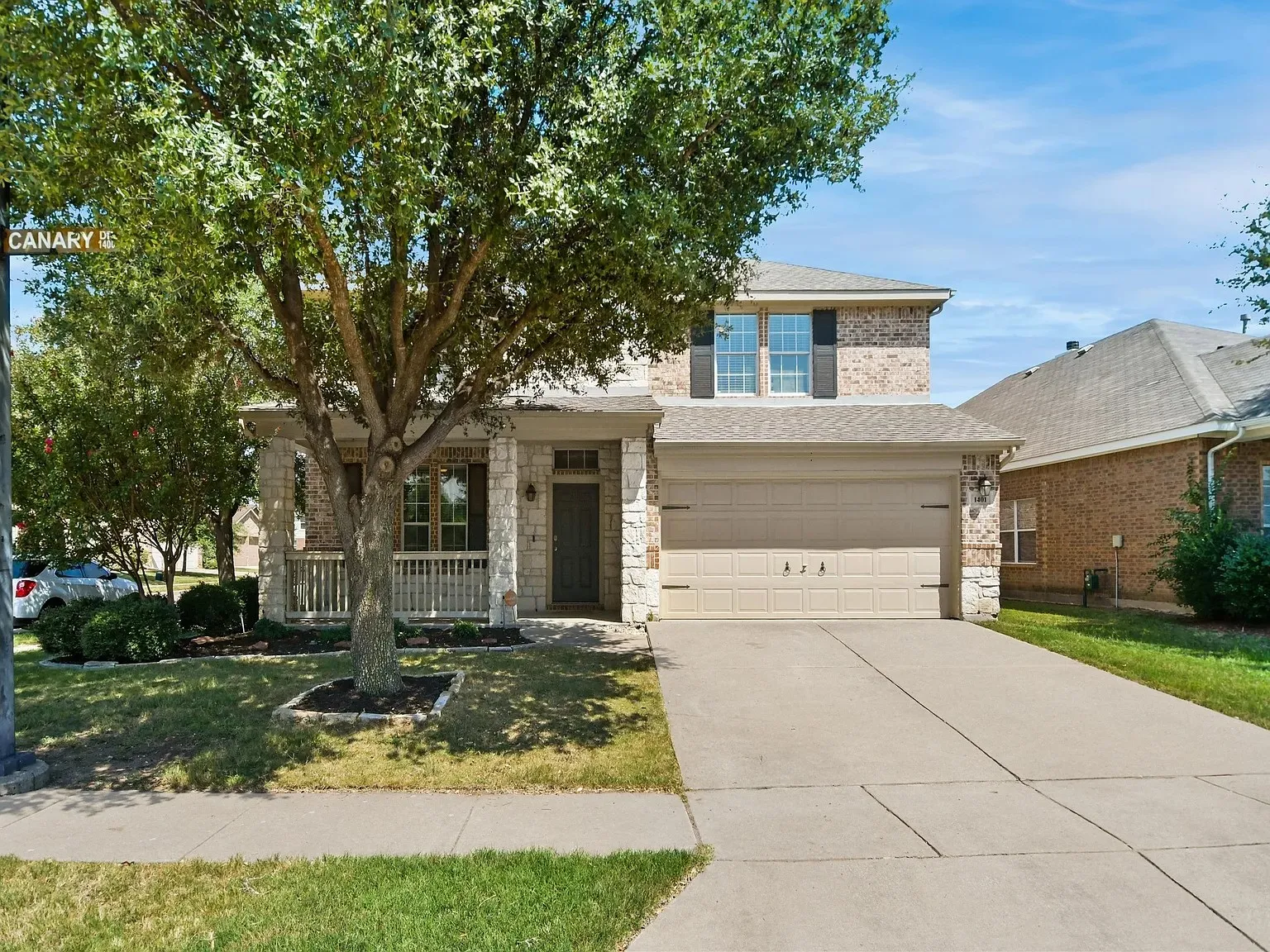 Two-story brick and stone exterior with a covered porch, attached garage, and concrete driveway