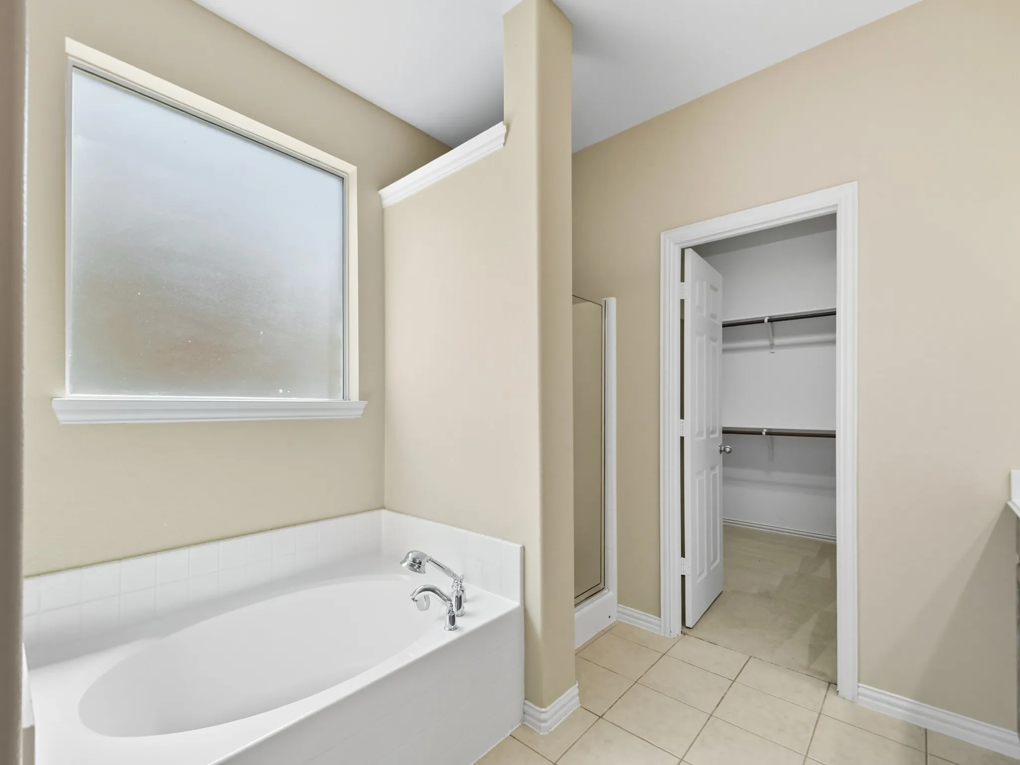 Primary Bathroom w Deep soaking tub with chrome fixtures, frosted glass window, tile flooring, and an open closet with shelving