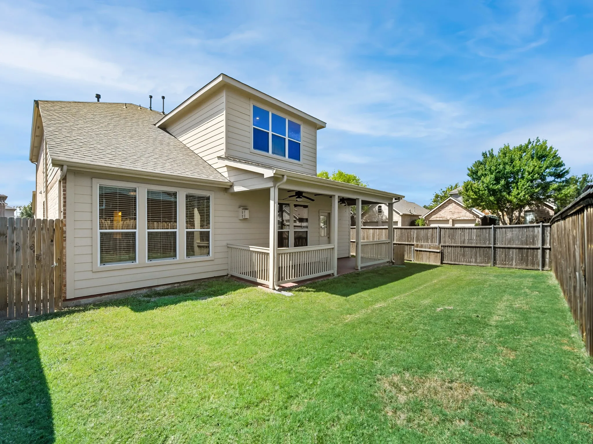 Expansive lawn with a wooden privacy fence, leading to a covered patio with a ceiling fan