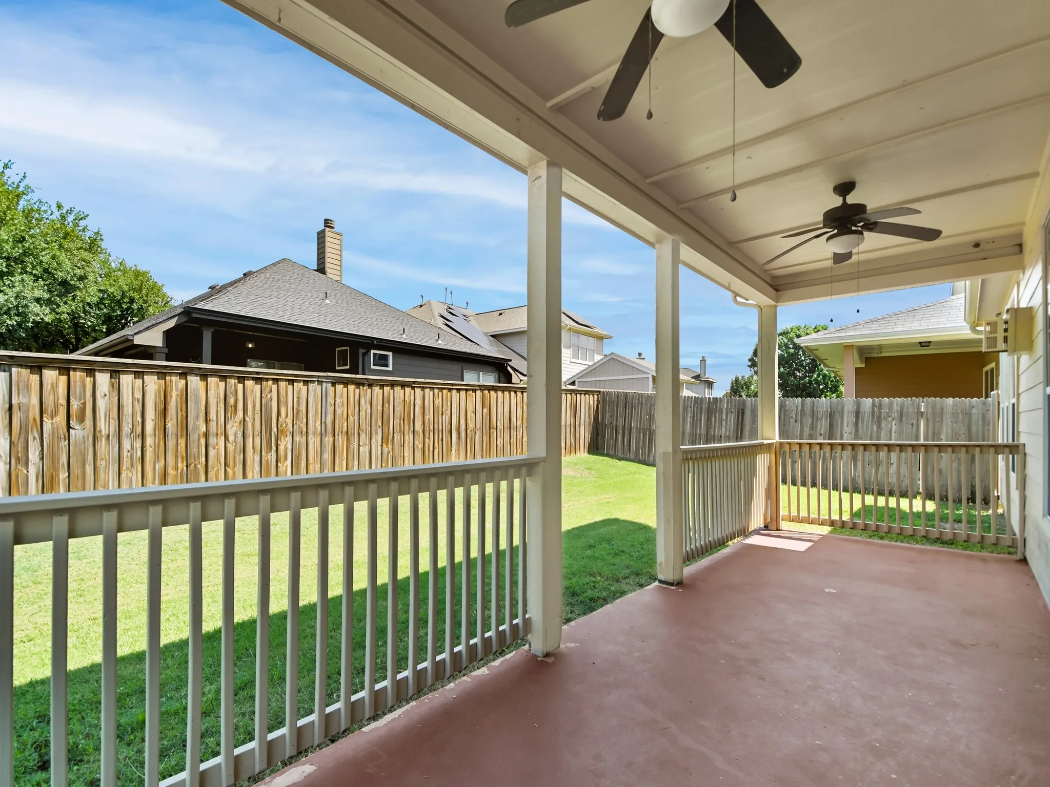 Covered patio with a painted concrete surface, white railing, and dual ceiling fans