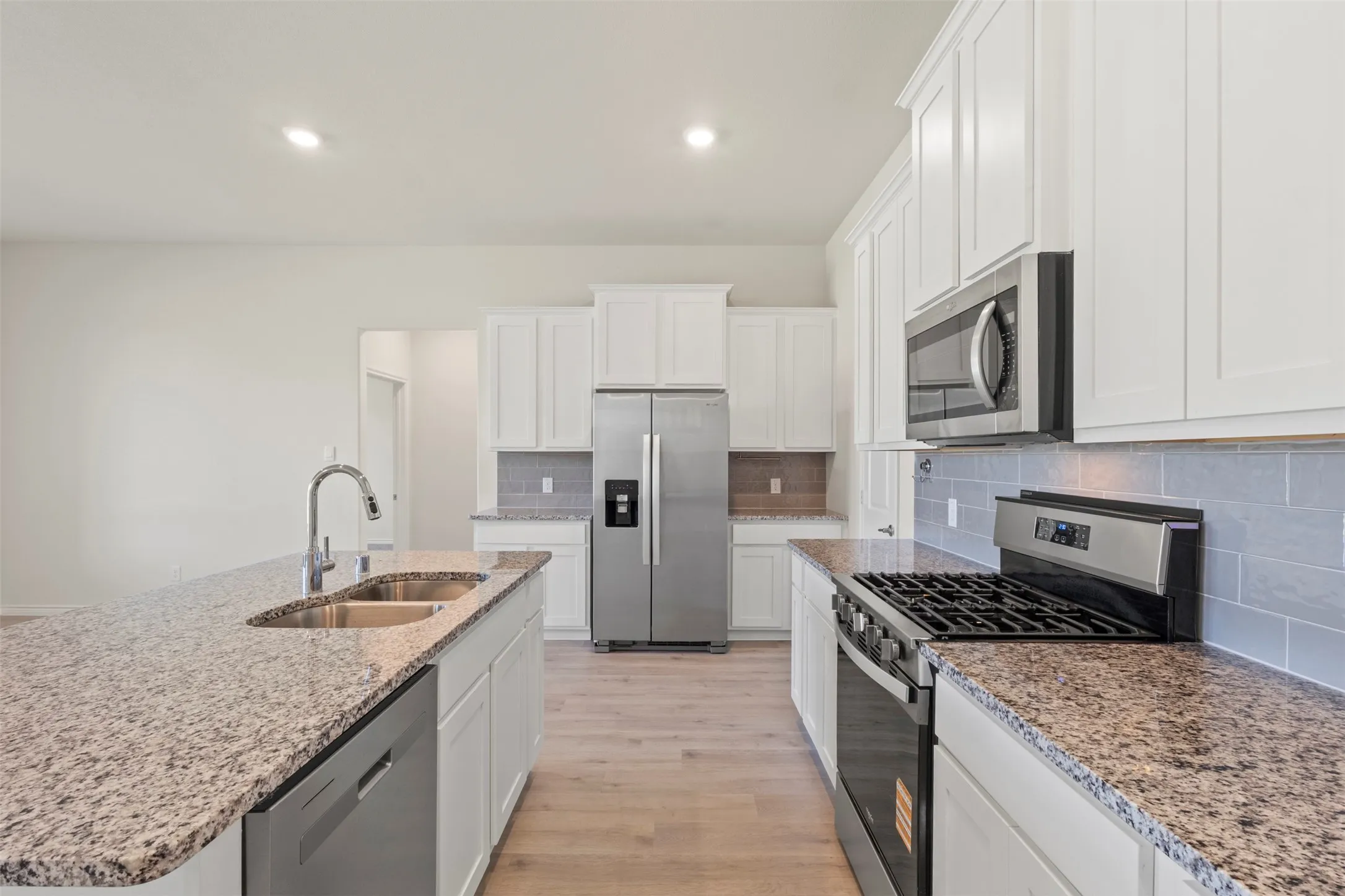 Kitchen featuring granite countertops, stainless steel appliances, white cabinetry, a double basin sink, and wood-finish flooring