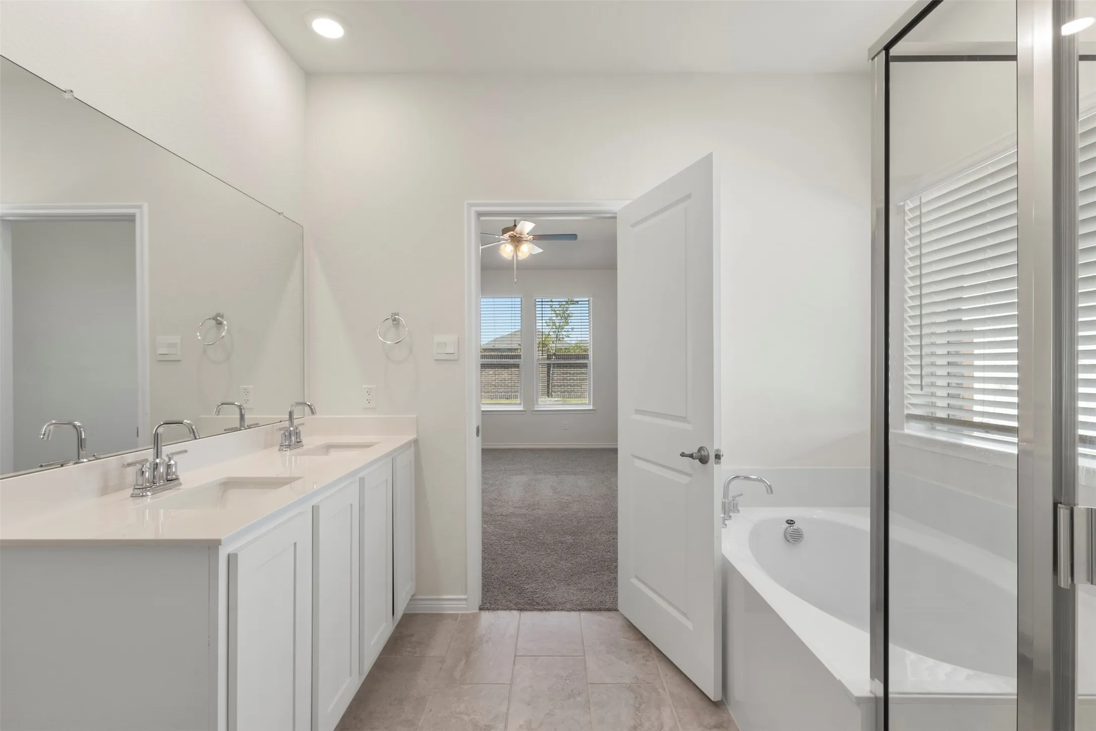 Dual sink vanity with white cabinetry, built-in bathtub, and walk-in shower with glass enclosure