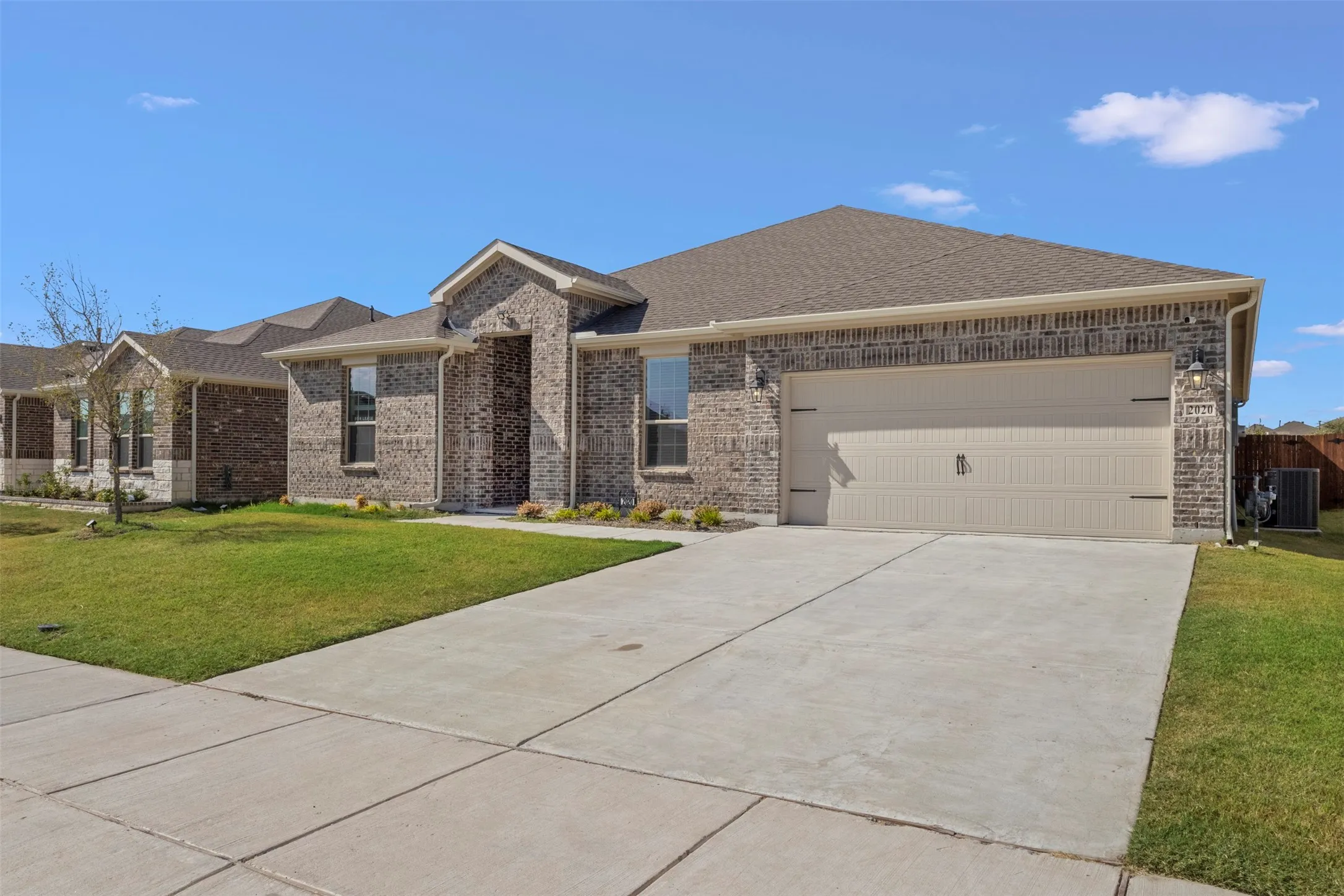 Brick exterior with stone accents, attached garage, concrete driveway, and a landscaped front yard
