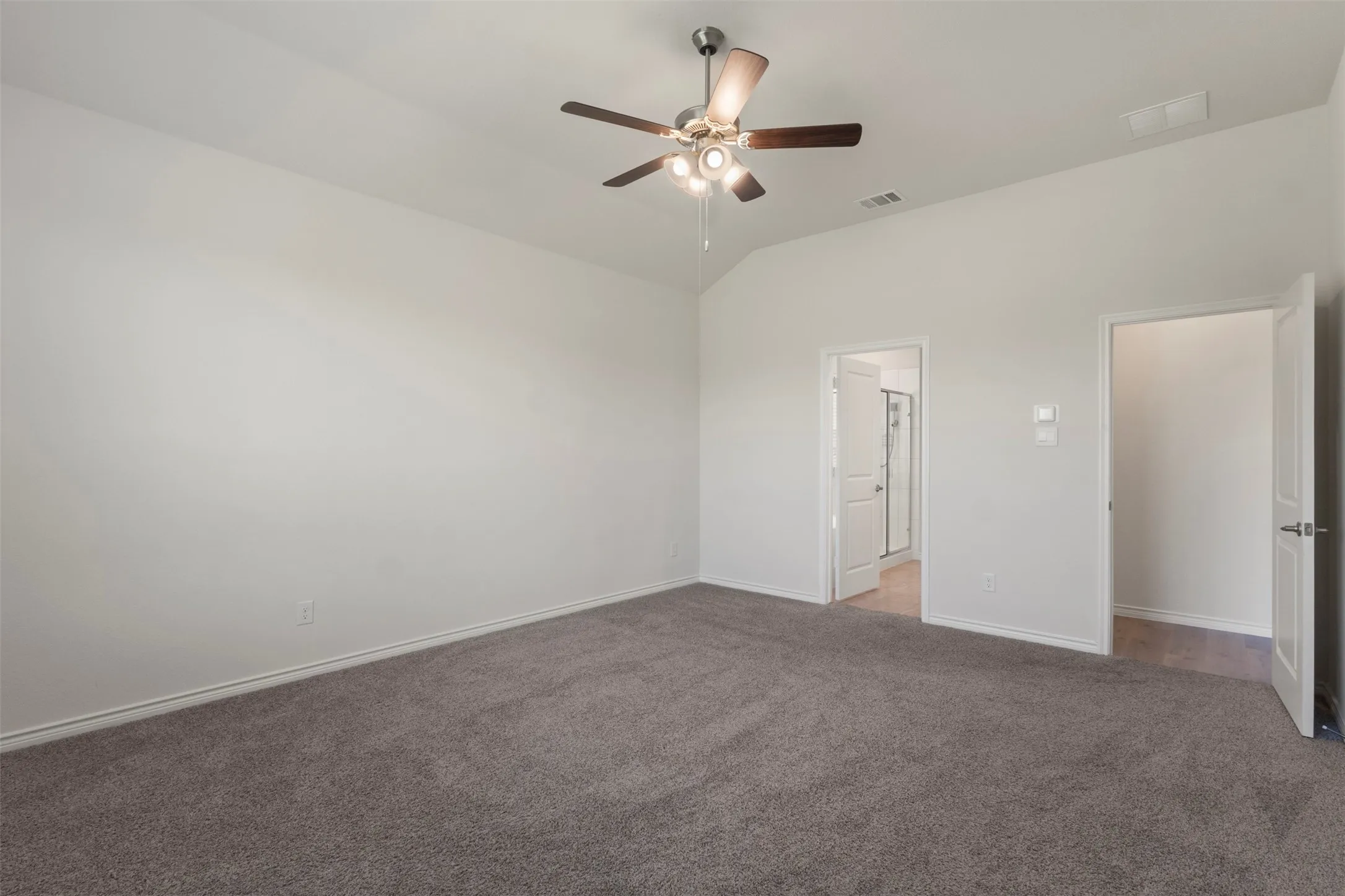 Carpeted room featuring vaulted ceilings, a ceiling fan with integrated lighting, and two doorways with white paneled doors