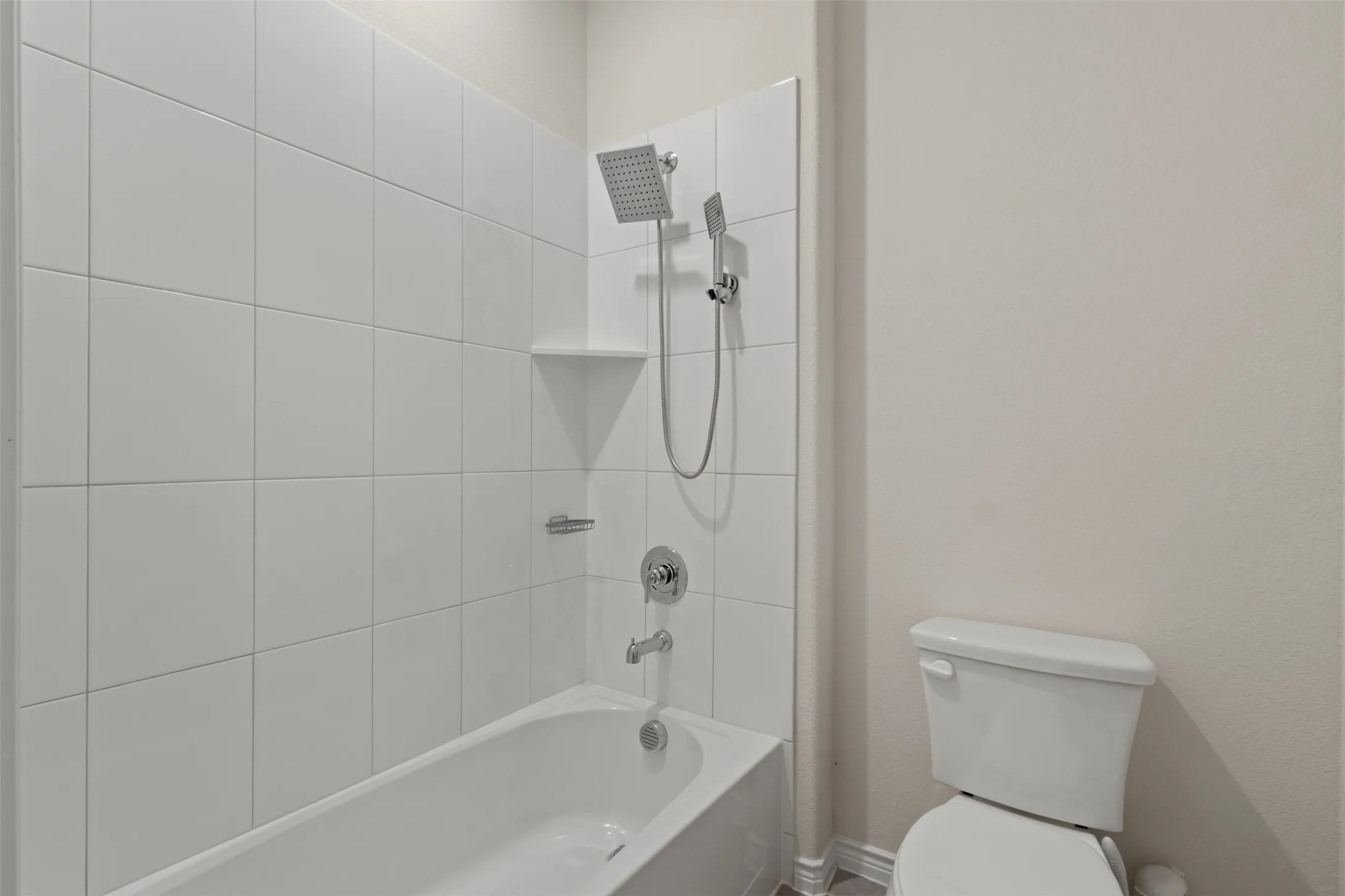 White tile shower surround with integrated shelving, chrome fixtures, and a white bathtub