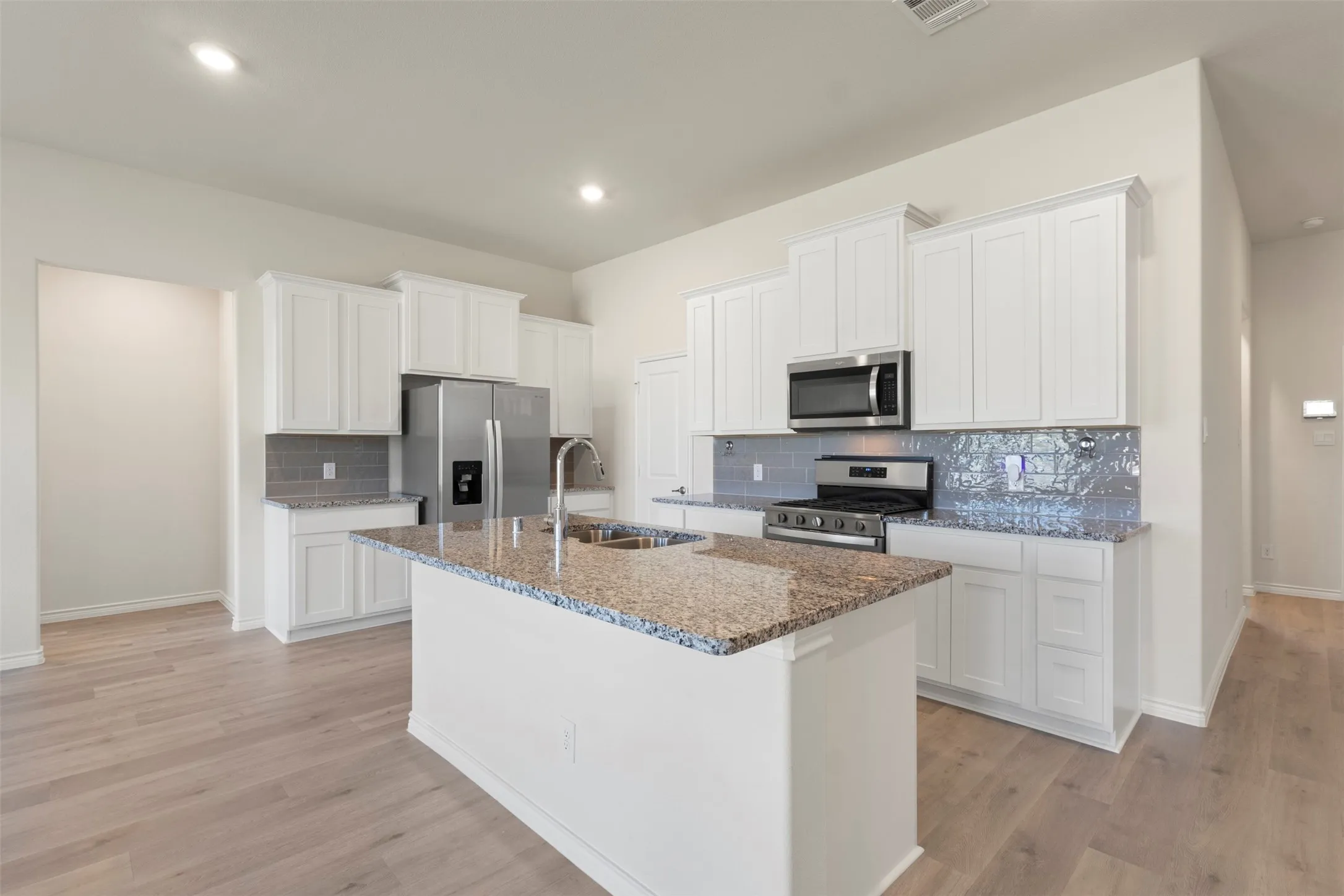 Kitchen featuring white cabinetry, stainless steel appliances, granite countertops, a center island with a sink, and wood-finish flooring