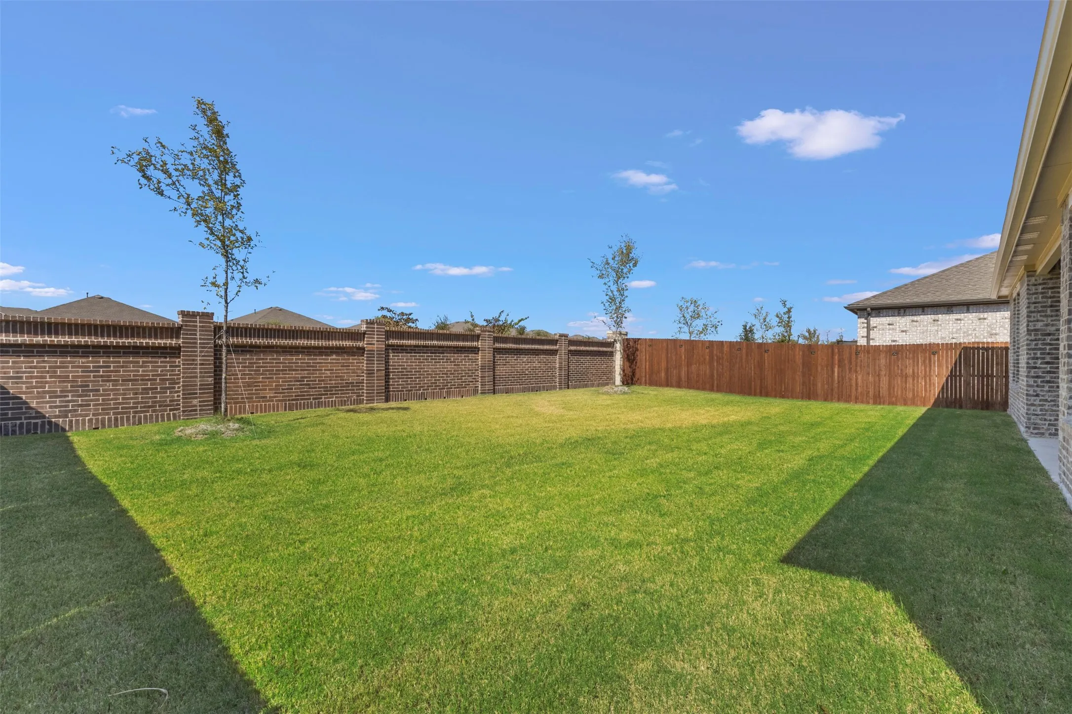 Expansive backyard with a lush lawn, featuring a brick perimeter fence with decorative pillars and a stained wood privacy fence