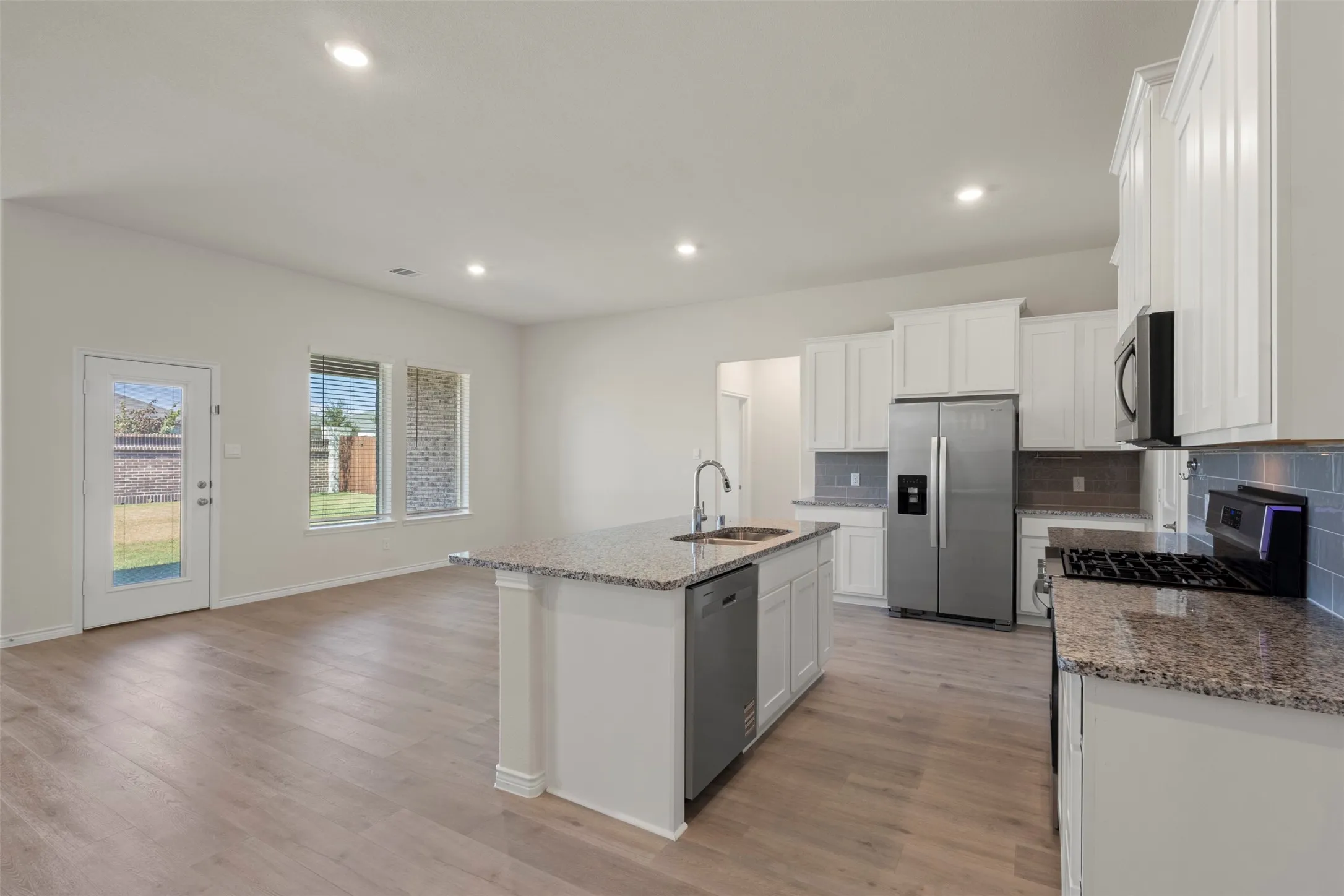 Open-concept kitchen featuring white cabinetry, stainless steel appliances, granite countertops, and a central island with sink