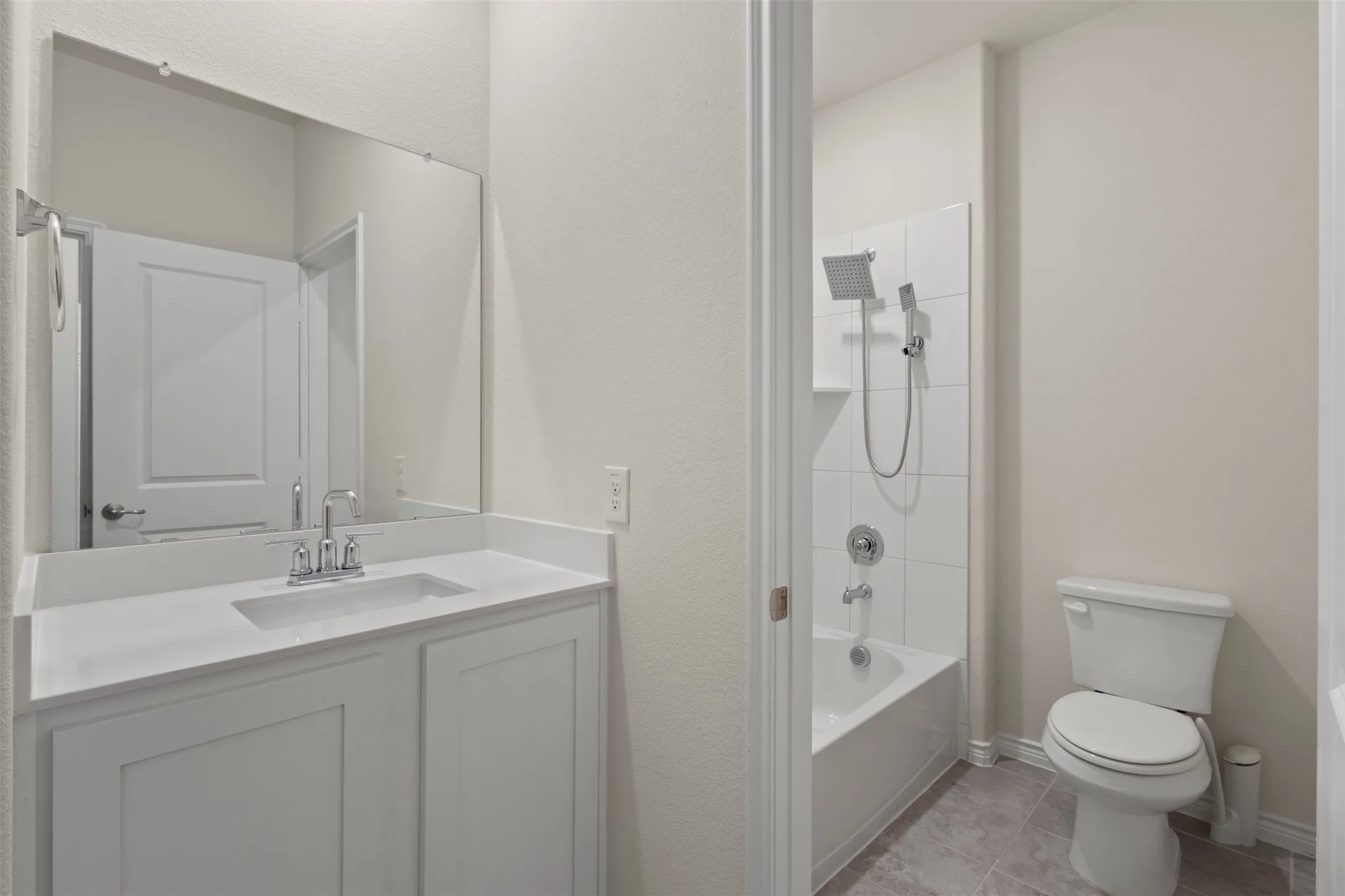 Vanity with an integrated sink and chrome faucet, large frameless mirror, white paneled cabinetry, and a full-size bathtub with a tiled shower surround