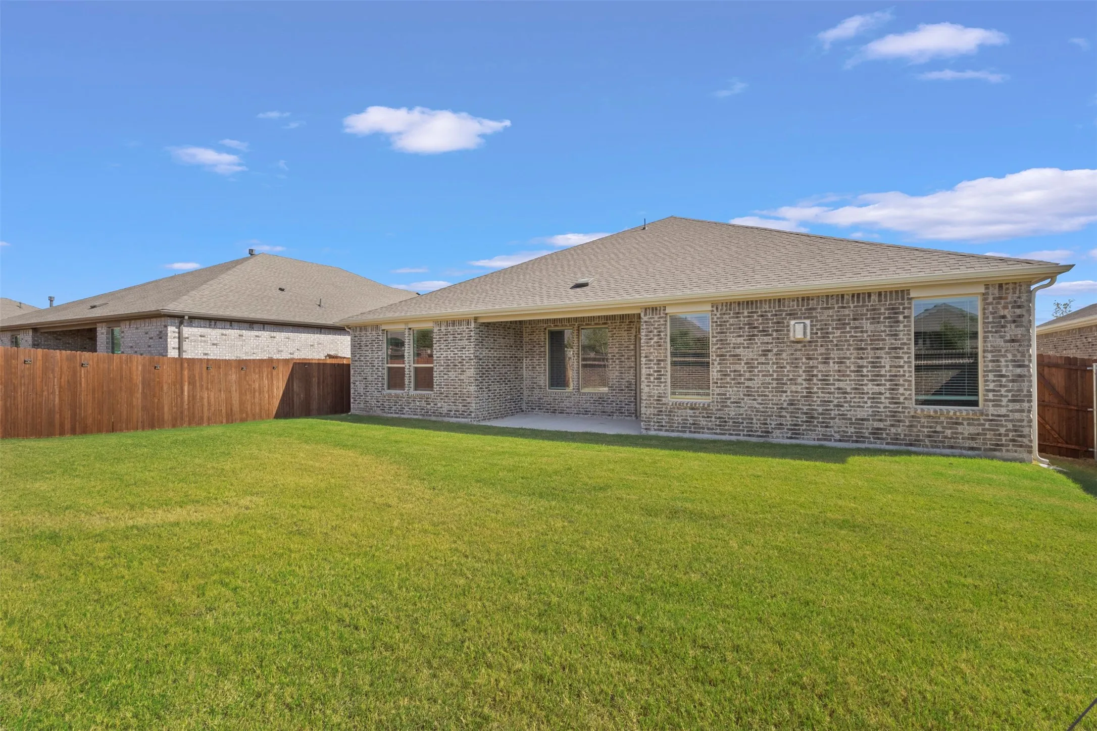 Expansive backyard with a manicured lawn, full brick exterior, covered patio, and privacy fencing