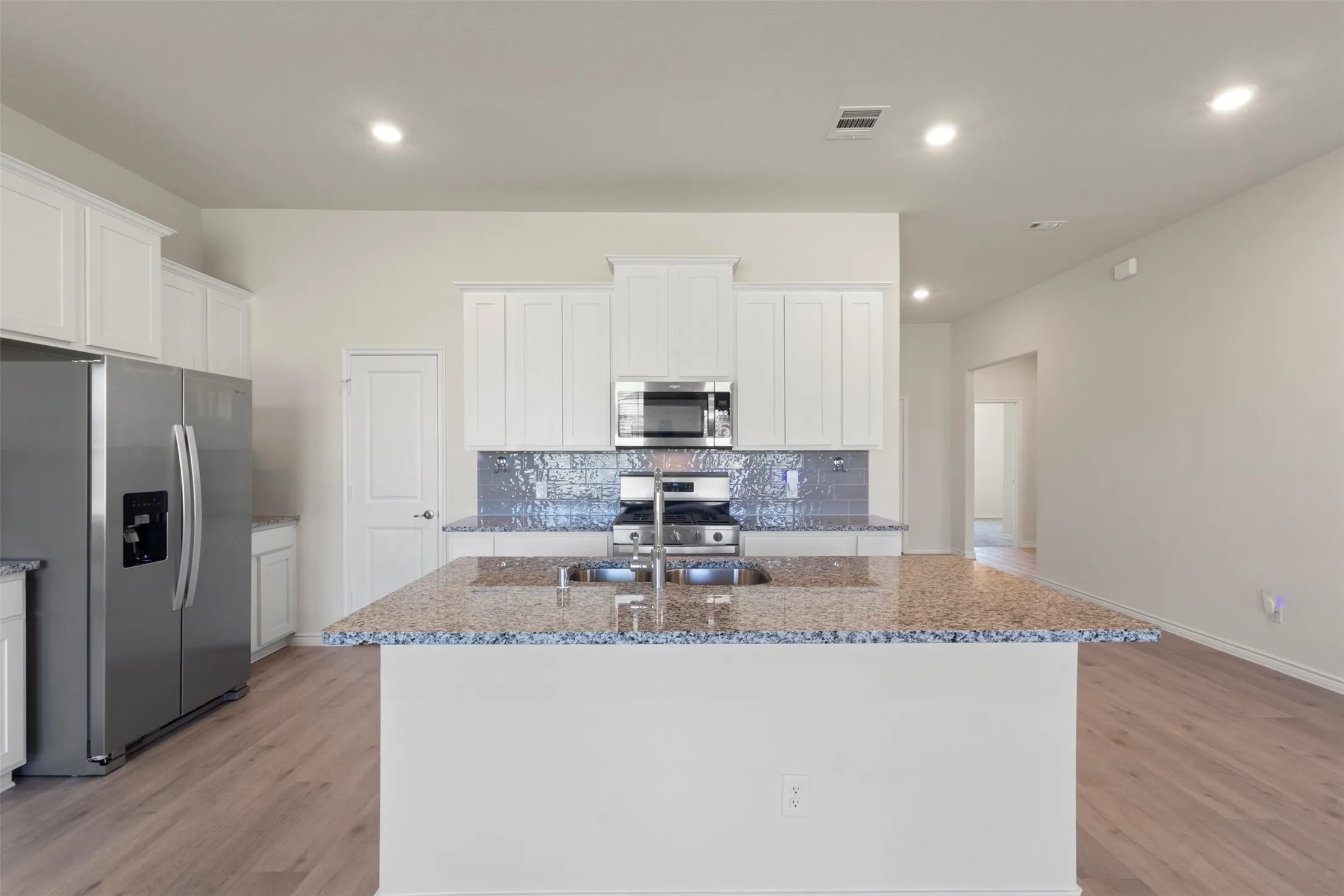 Kitchen featuring an expansive island with a granite countertop, stainless steel appliances, white cabinetry, and wood-finish flooring