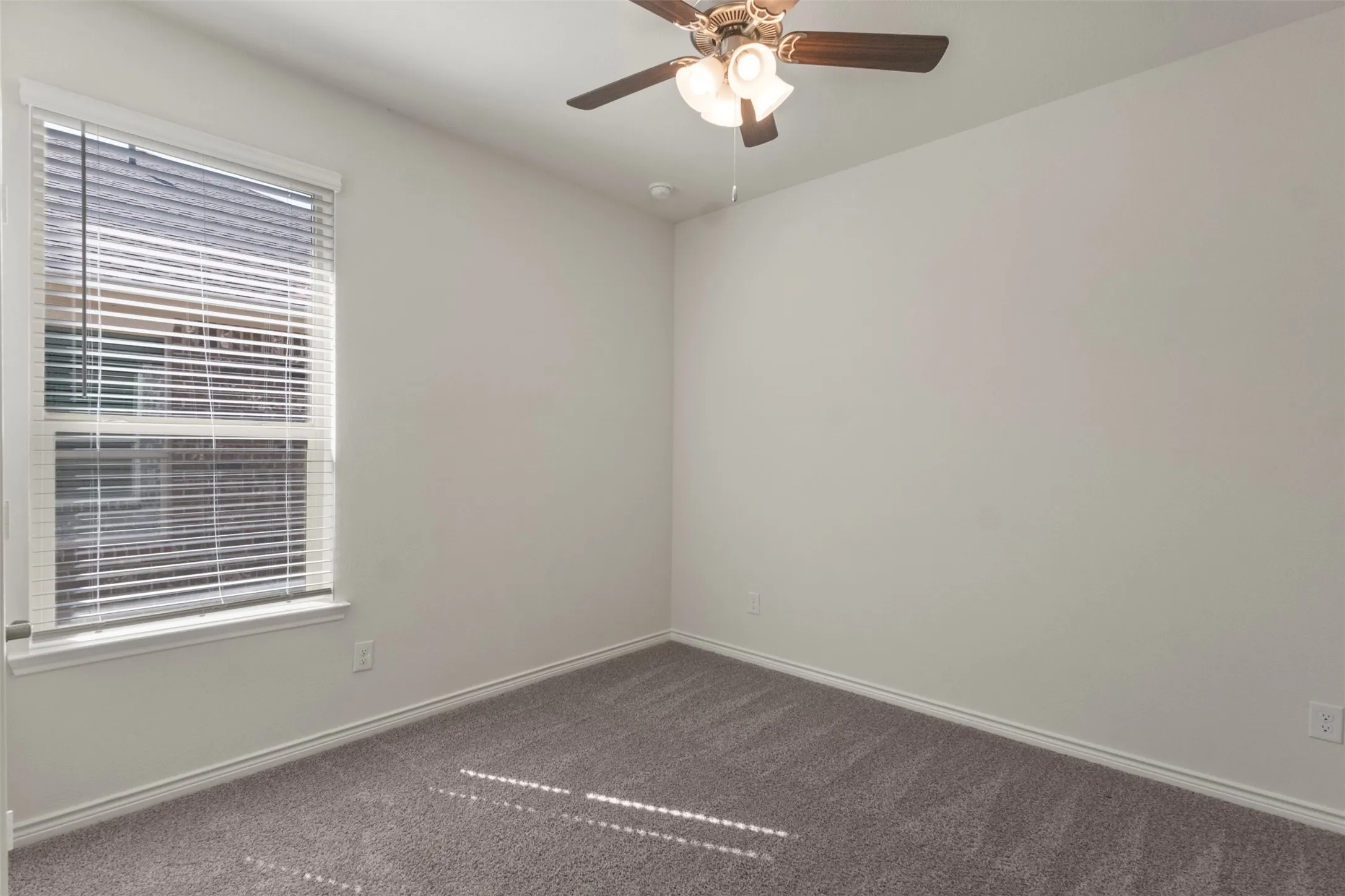 Neutral wall paint, window with blinds, ceiling fan with light fixture, and gray carpeting