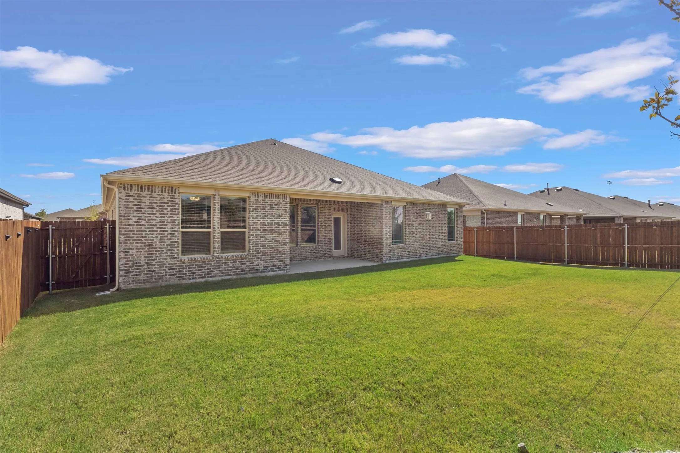 Expansive backyard with a manicured lawn, full perimeter privacy fencing, and a concrete patio