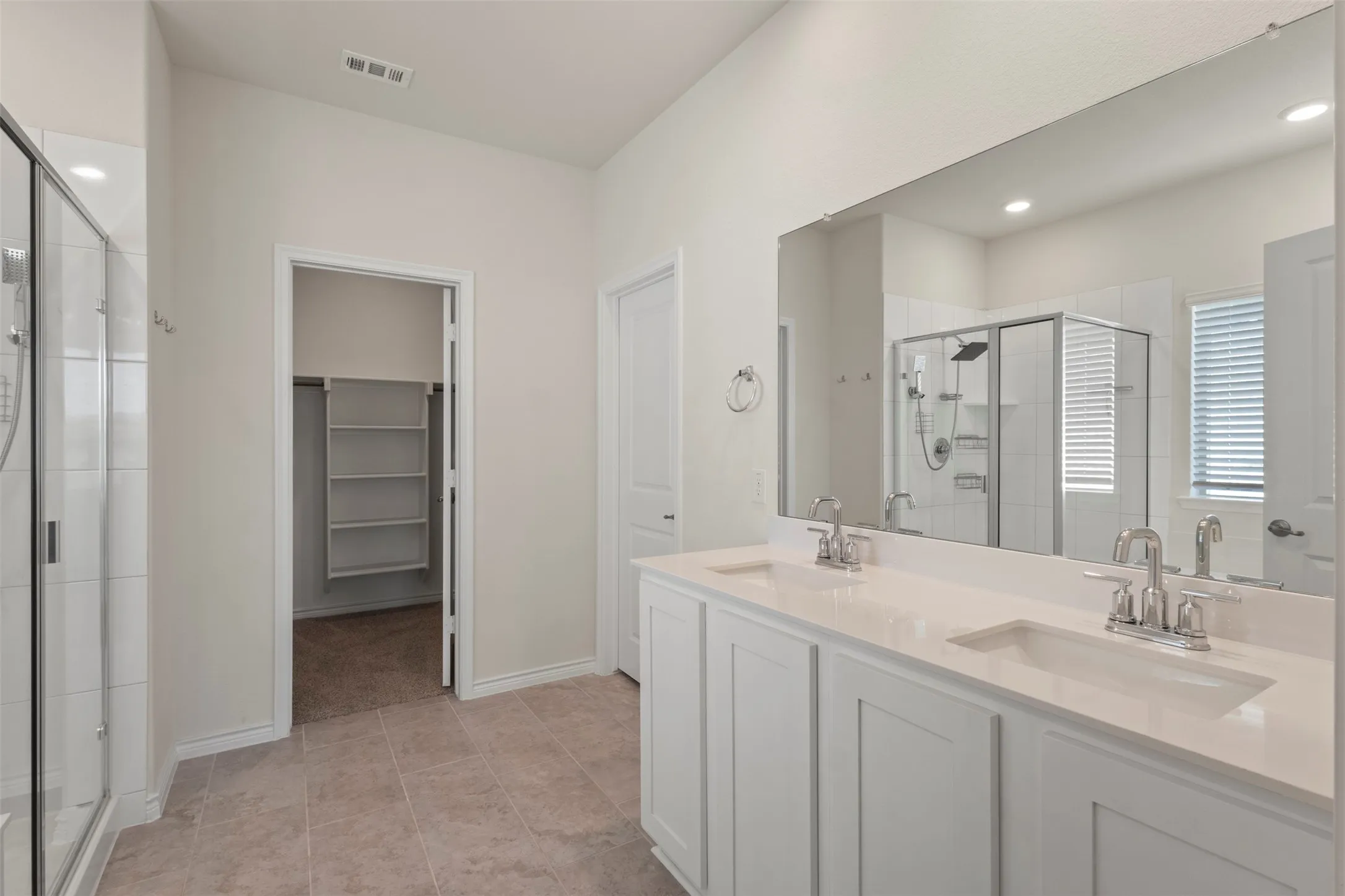 Double vanity with white cabinetry and integrated sinks, a glass-enclosed shower, tile flooring, and a walk-in closet with built-in shelving