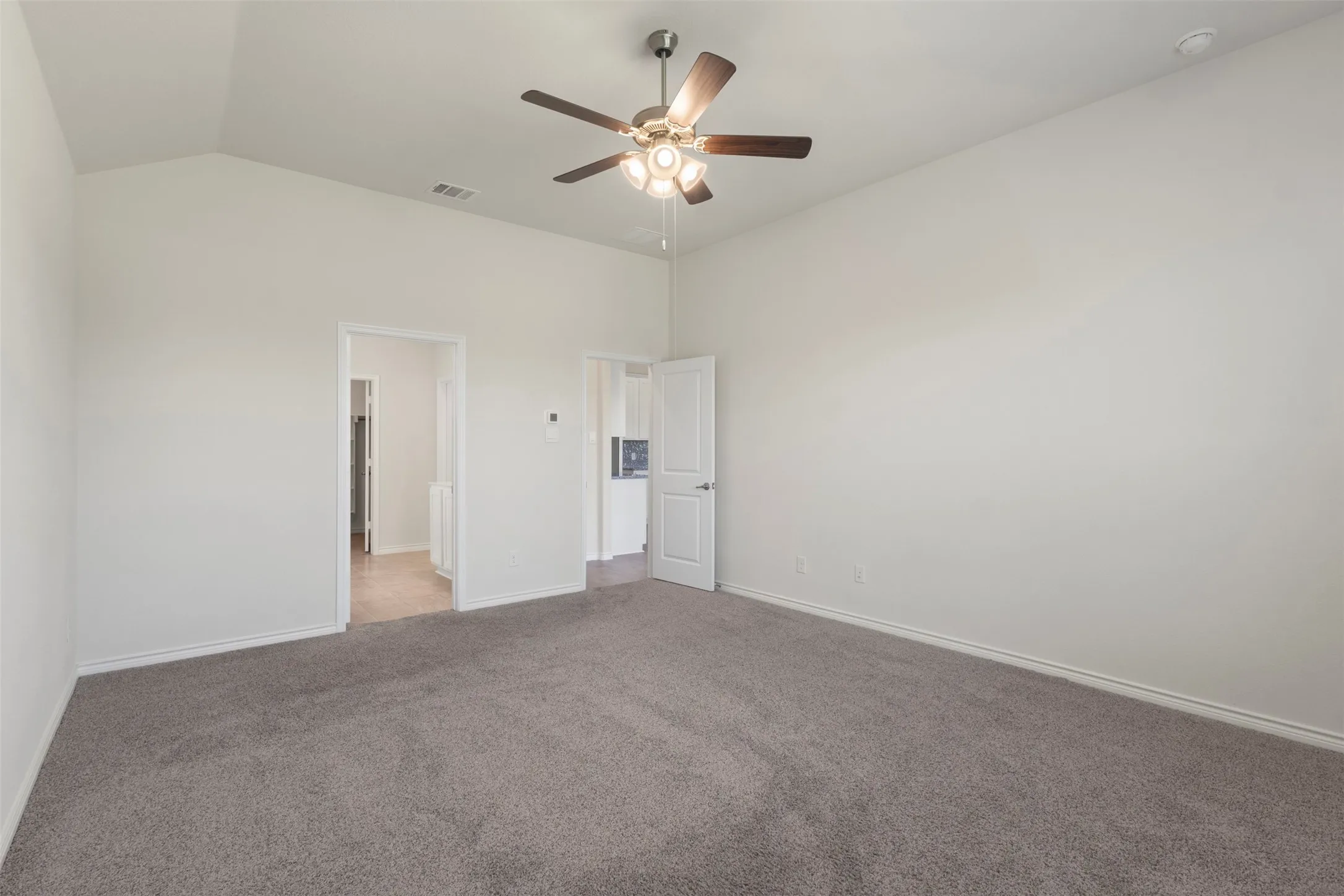 Vaulted ceiling with an attached ceiling fan, plush carpet, and white interior doors