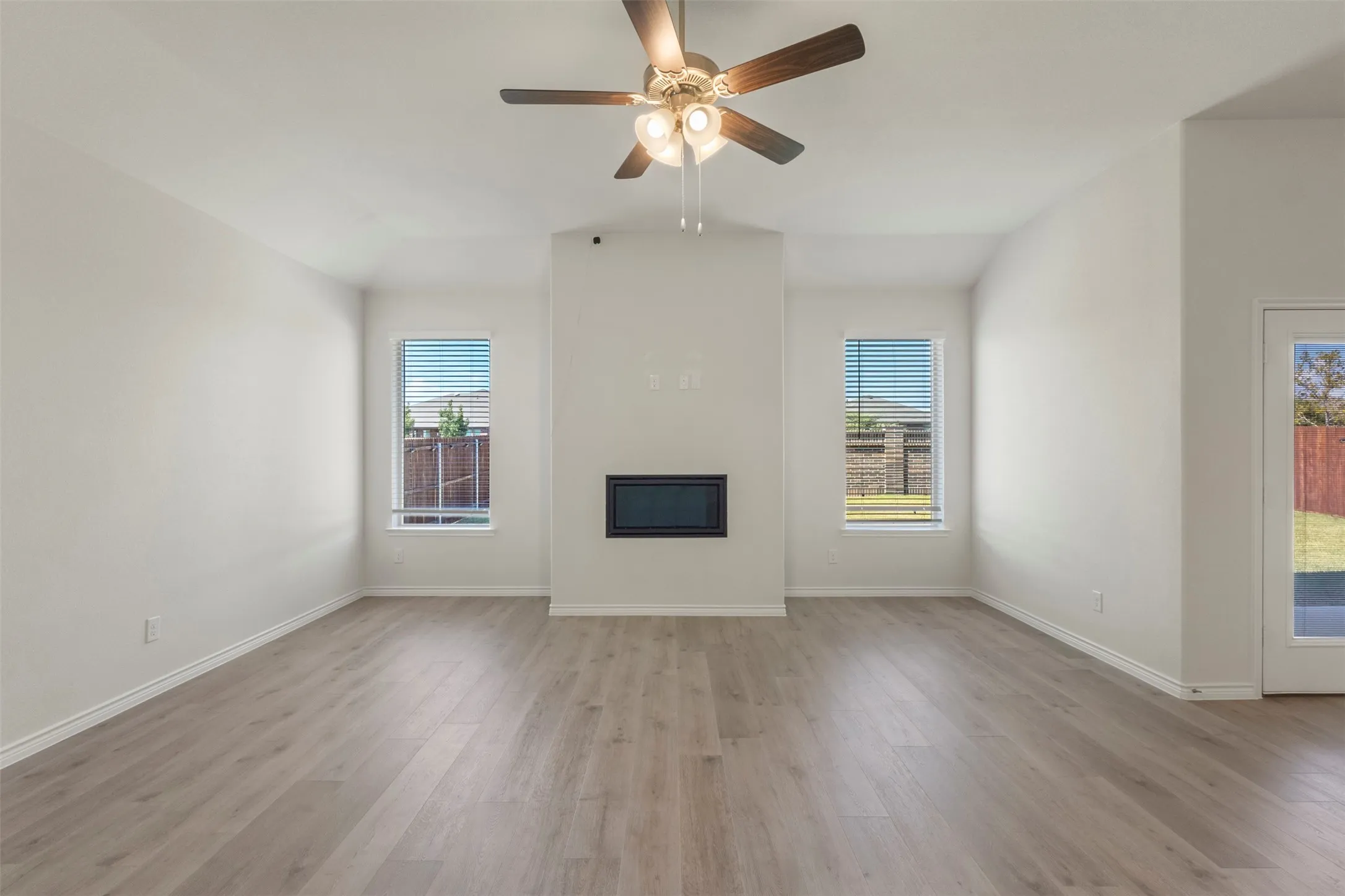 Spacious room with high ceilings, wood-finish flooring, a built-in fireplace, and overhead ceiling fan