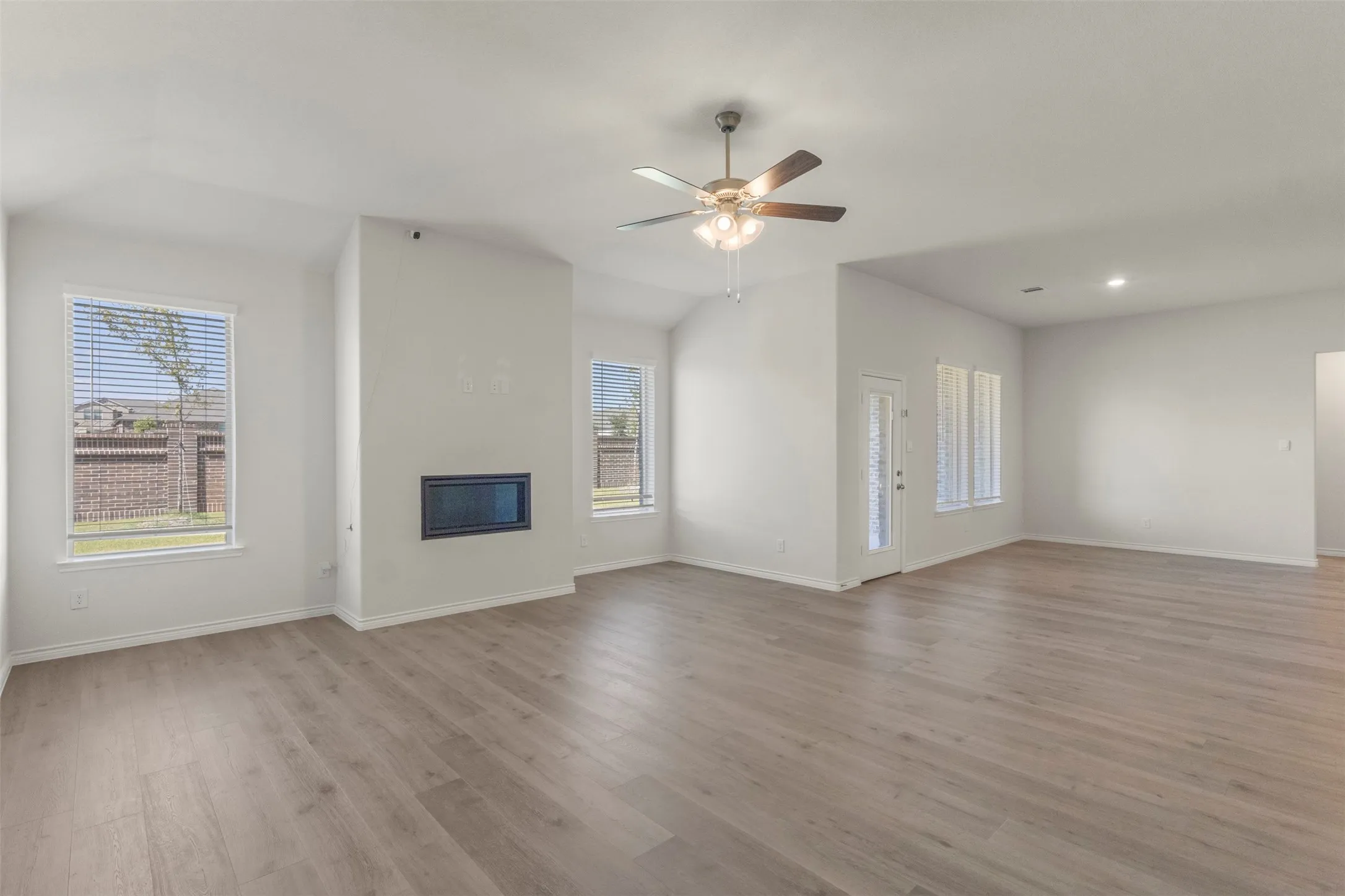 Vaulted ceiling living area featuring wood-finish flooring, a modern fireplace, multiple windows with blinds, and a ceiling fan
