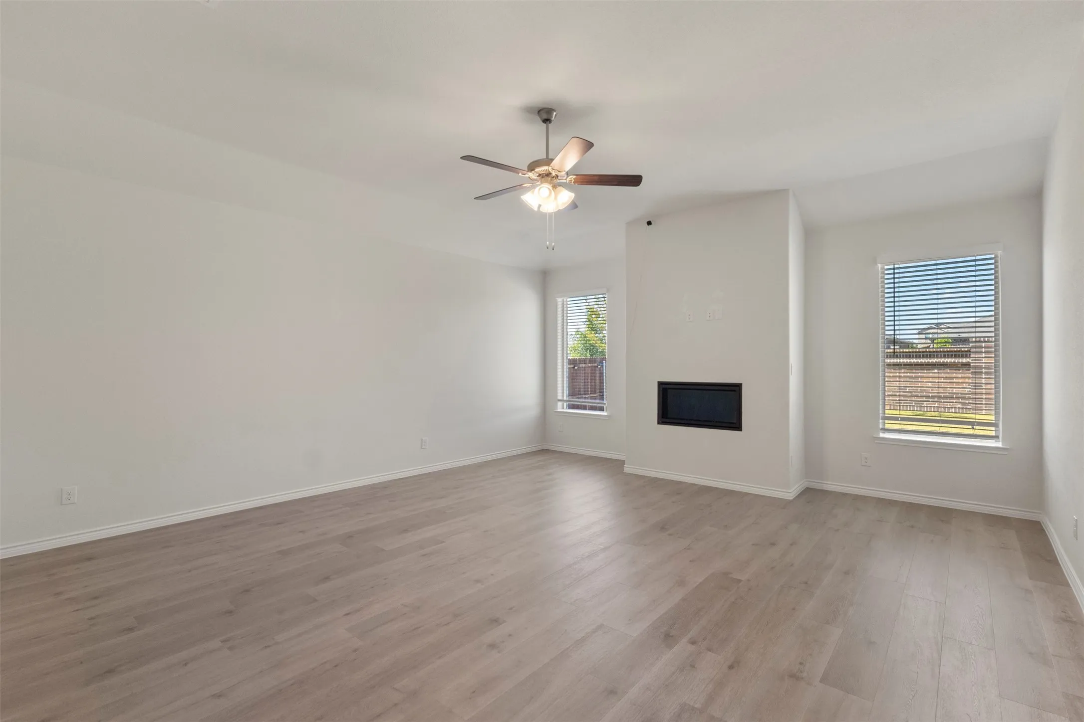 Spacious room featuring wood-finish flooring, an in-wall fireplace, multiple windows, and a ceiling fan