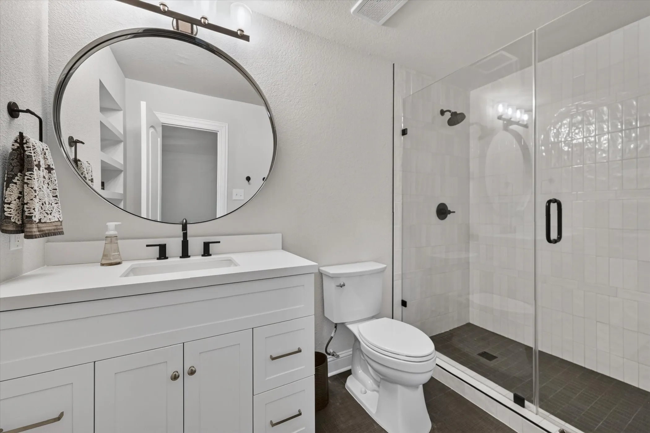 White vanity with a rectangular undermount sink, matte black faucet, and a round mirror