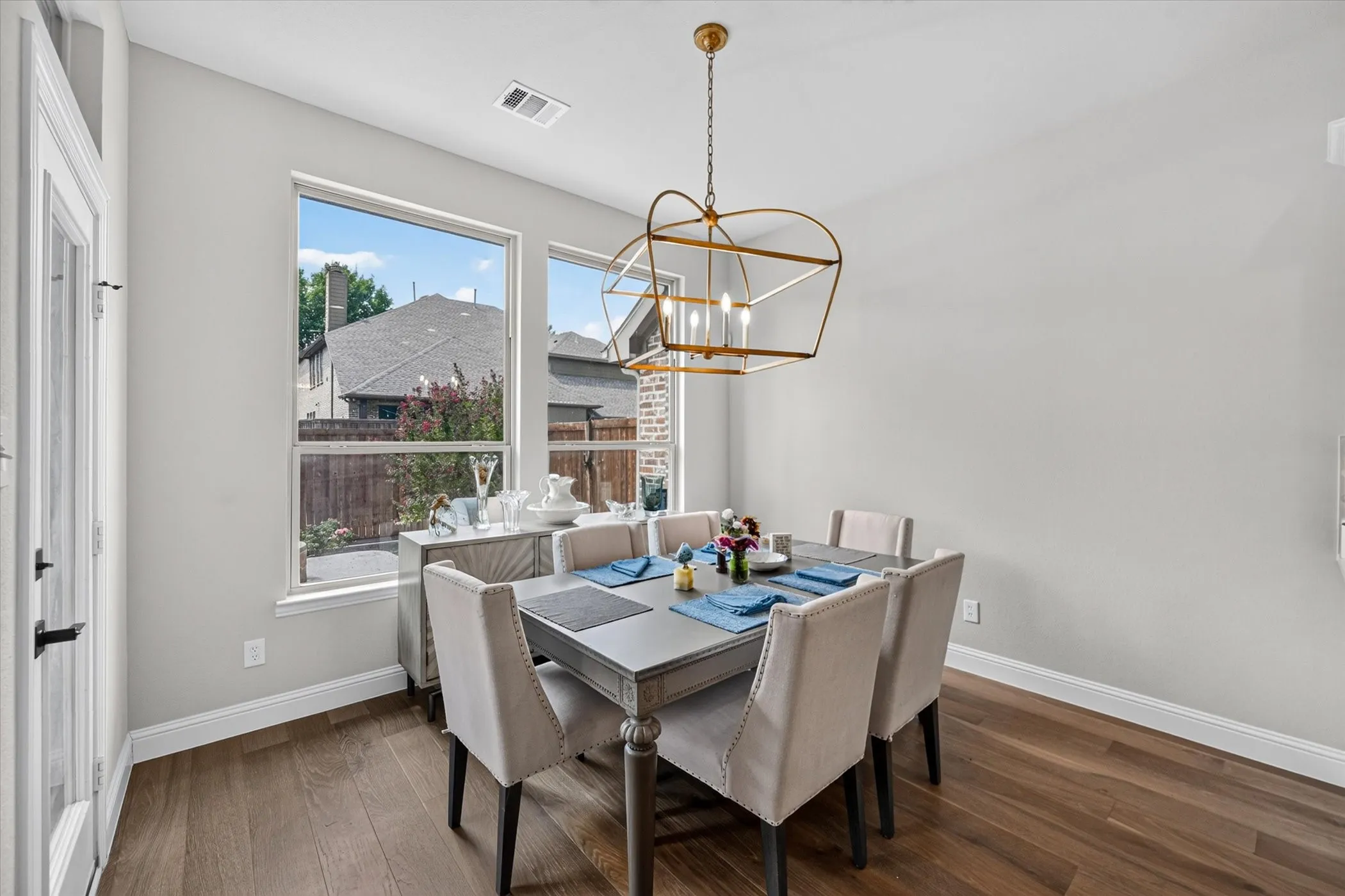 Wood-finish flooring with a modern open cage chandelier, complemented by multiple windows and a glass-paneled door