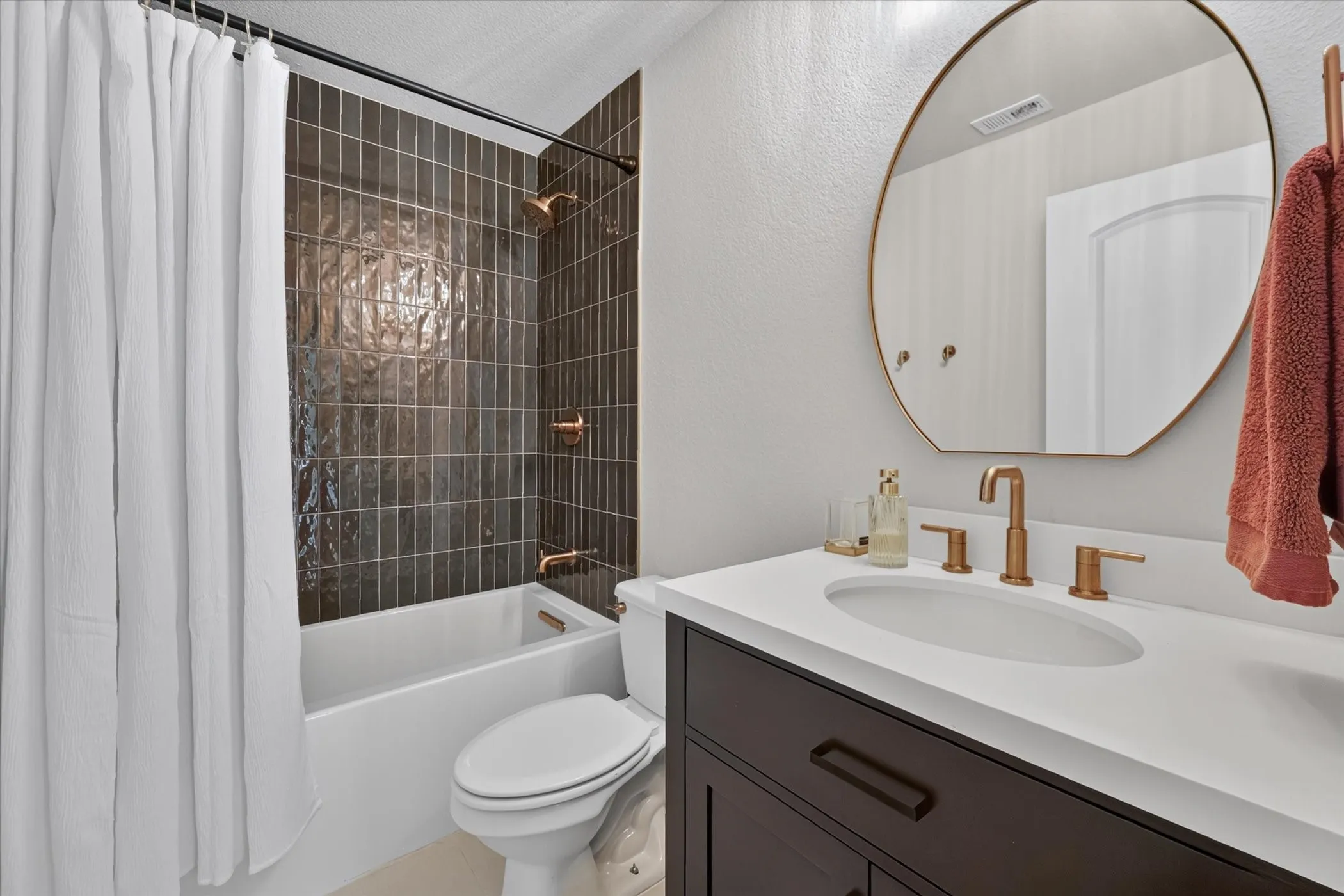 Recessed bathtub with dark subway tile surround, white vanity countertop, oval under-mount sink, and bronze-finish fixtures