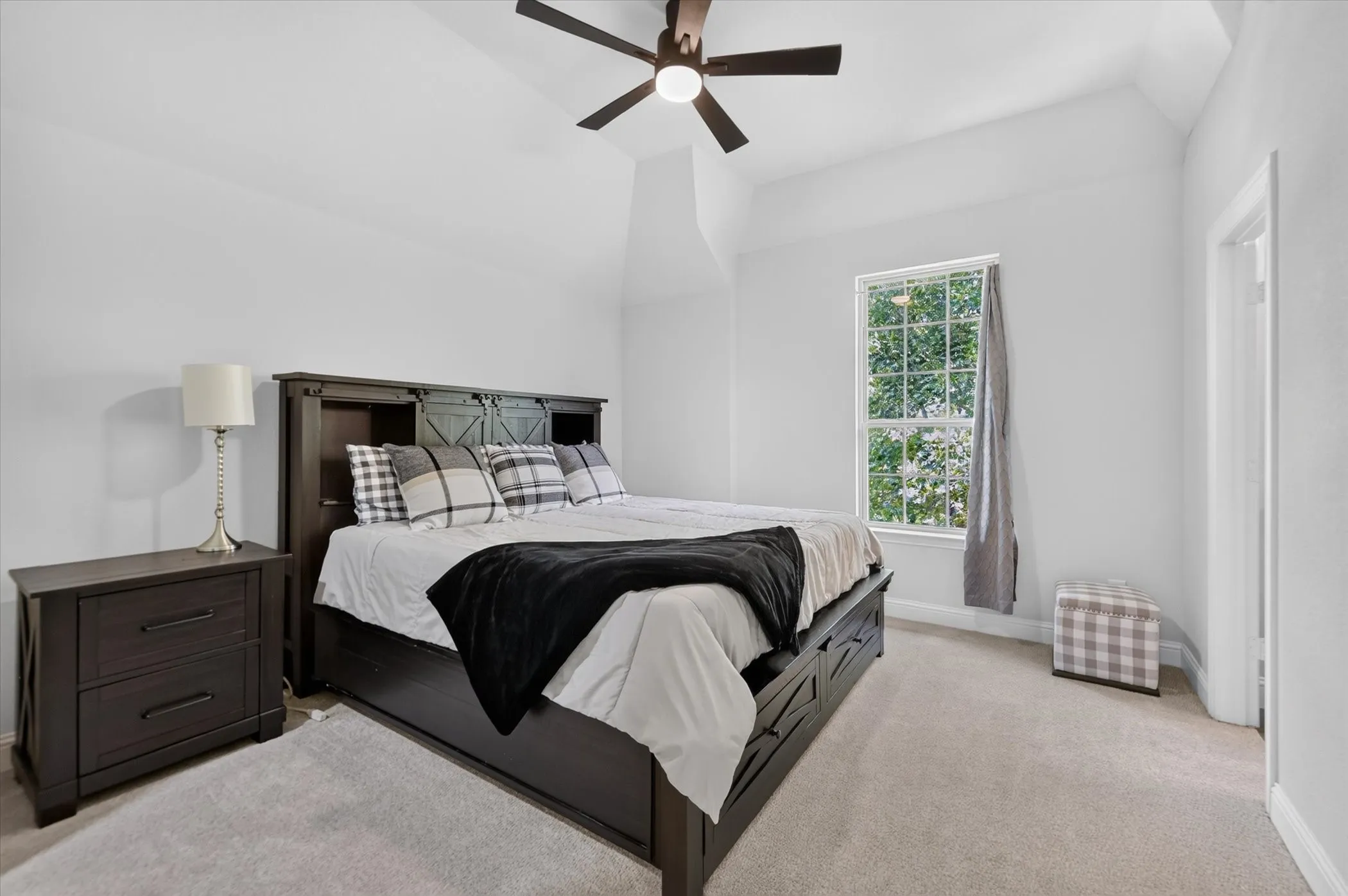 Vaulted ceiling with a ceiling fan, window with natural light, and soft-toned carpeting