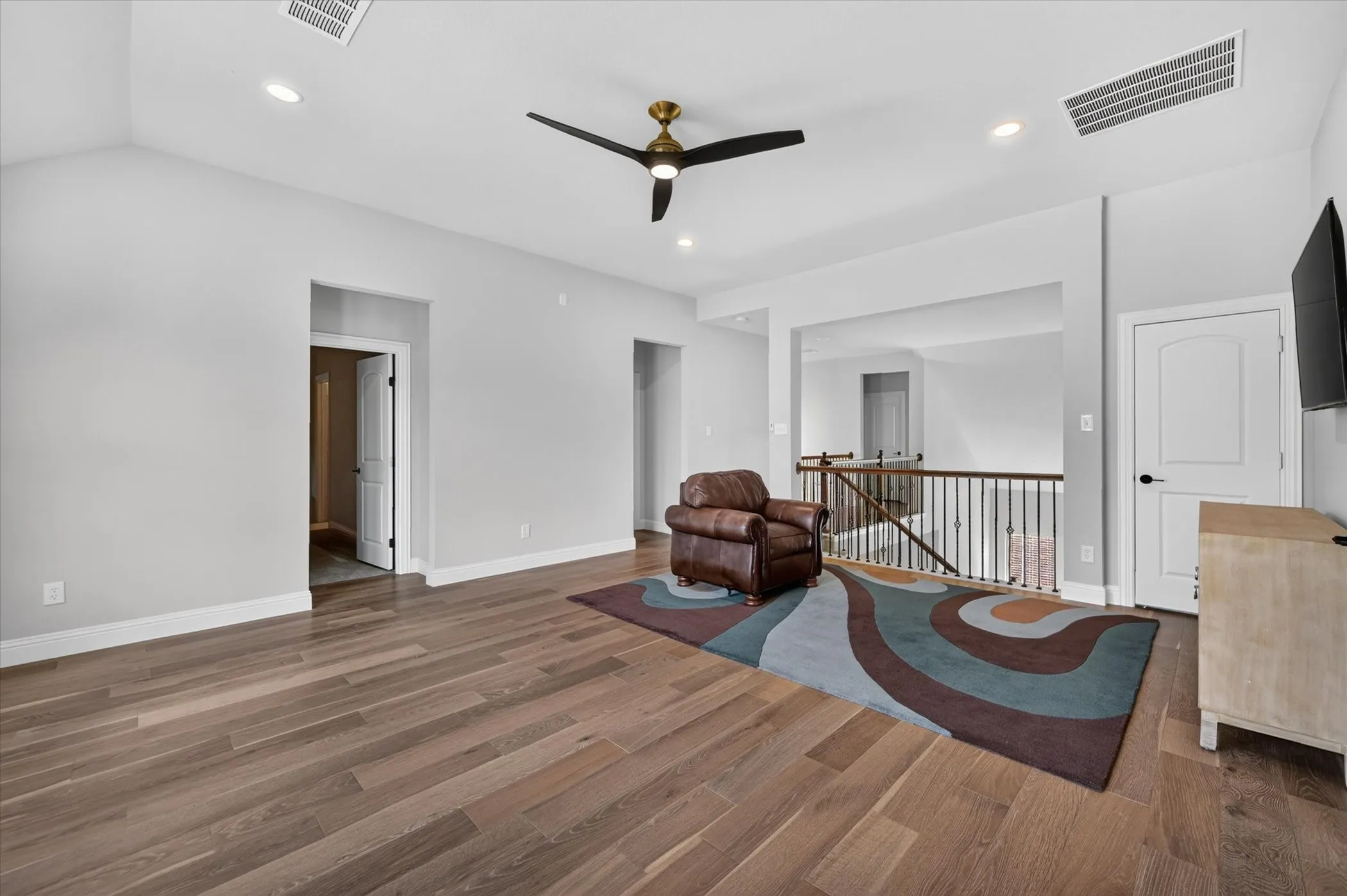 Spacious room featuring wood-finish flooring, recessed lighting, a ceiling fan with a brass-finish motor, and an open railing overlooking a lower level