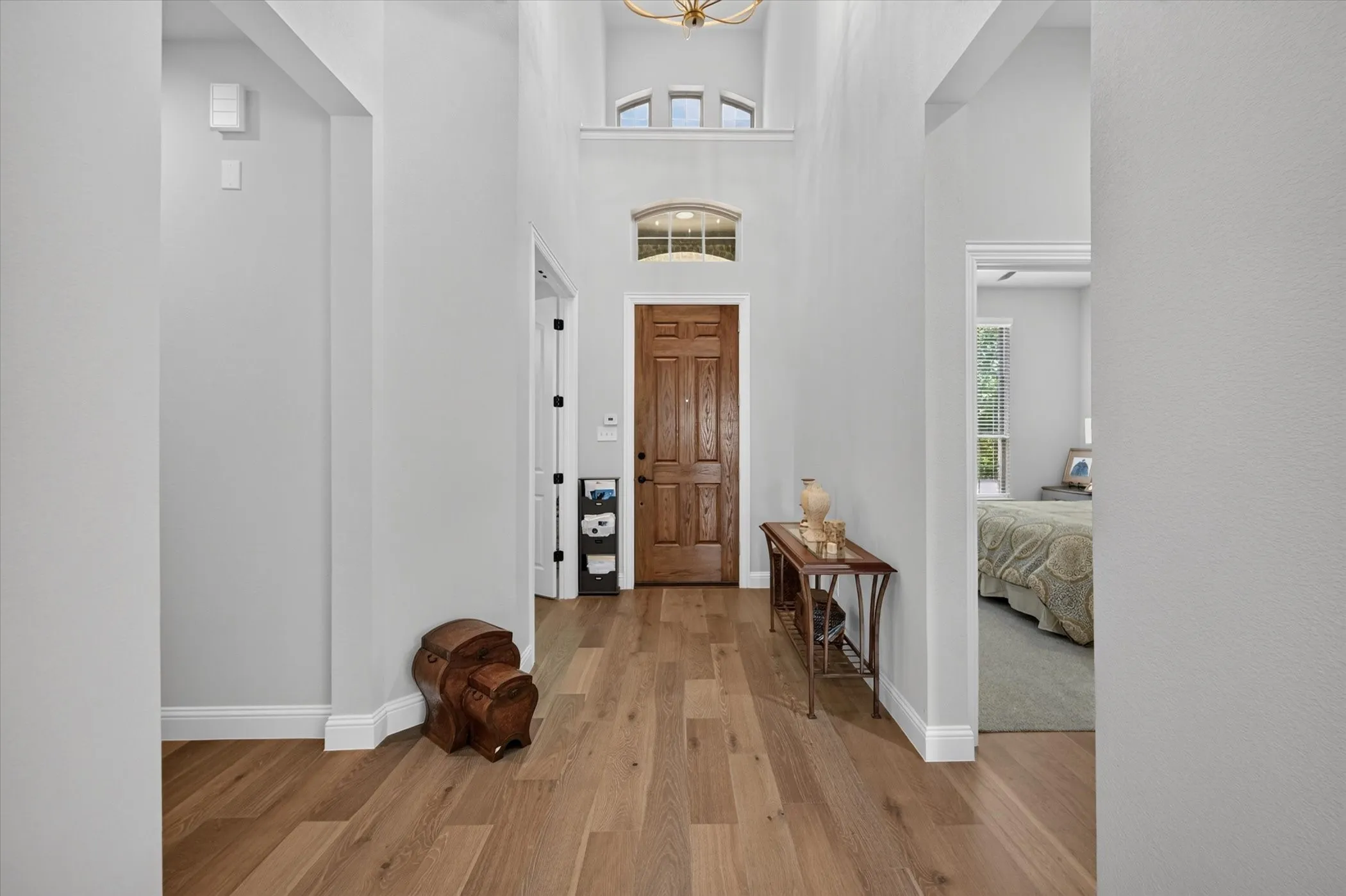 Double-height foyer featuring wood-finish flooring, a solid wood entry door, an arched transom window, and a multi-tiered ceiling