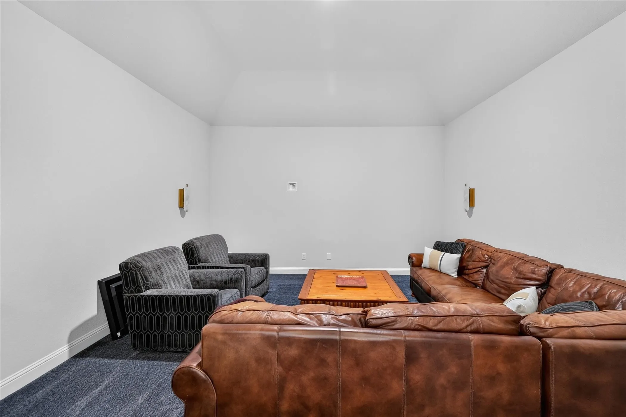 Vaulted ceiling, wall-mounted sconces, and dark carpeting