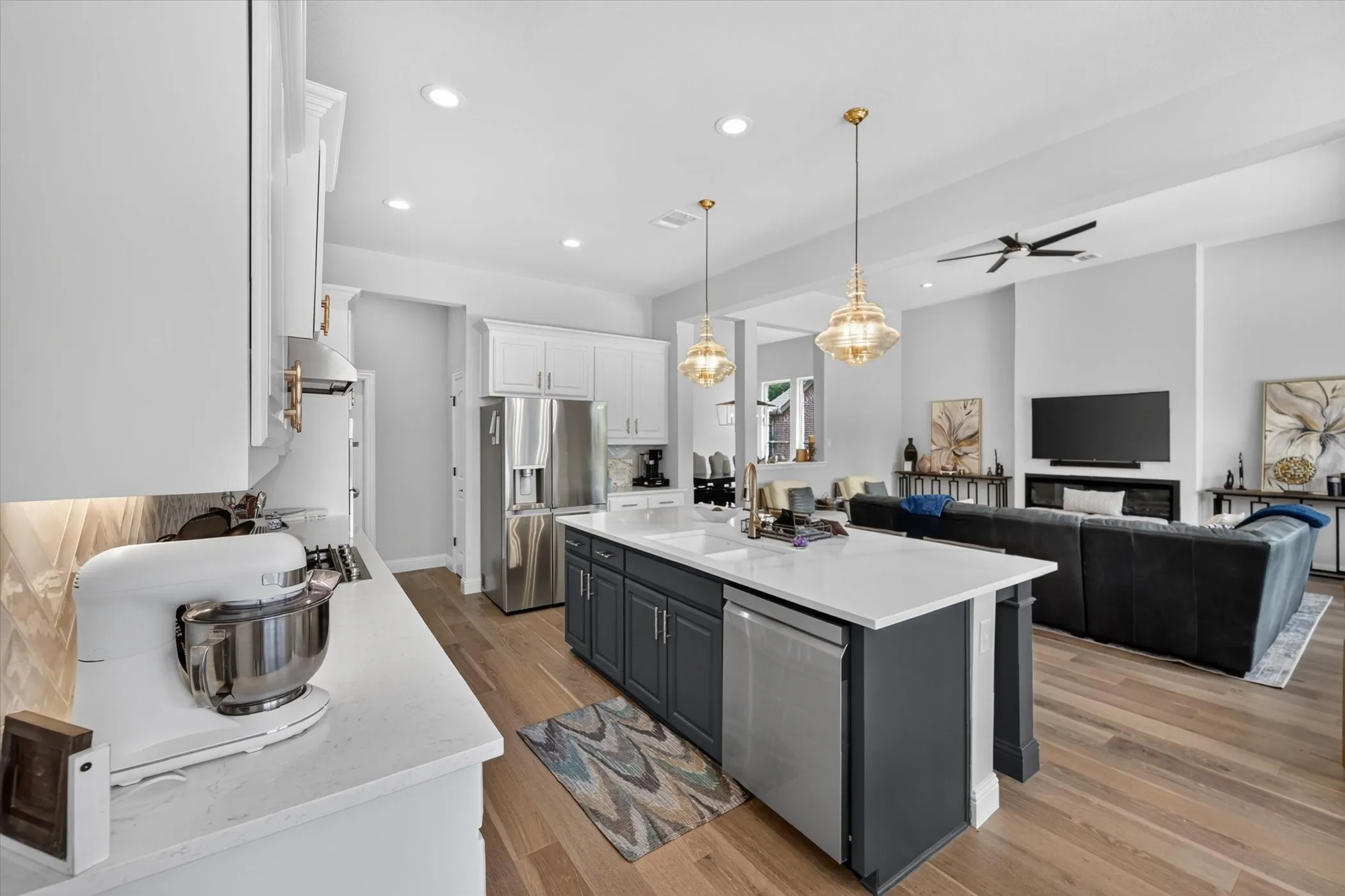 Spacious kitchen featuring an island with a built-in sink and dishwasher, stainless steel appliances, white cabinetry, and wood-finish flooring