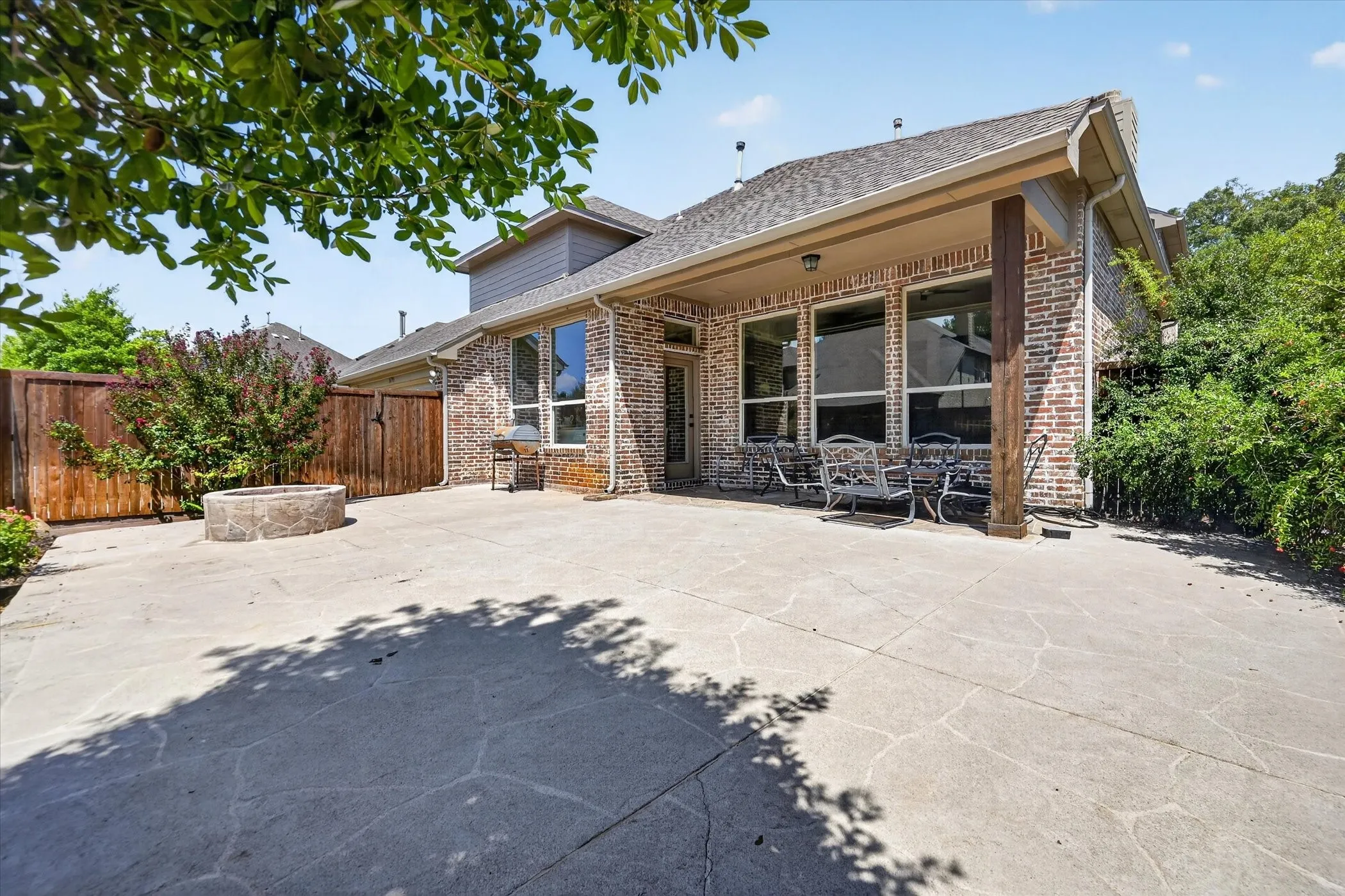 Expansive concrete patio with a built-in fire pit, covered patio area, and brick exterior