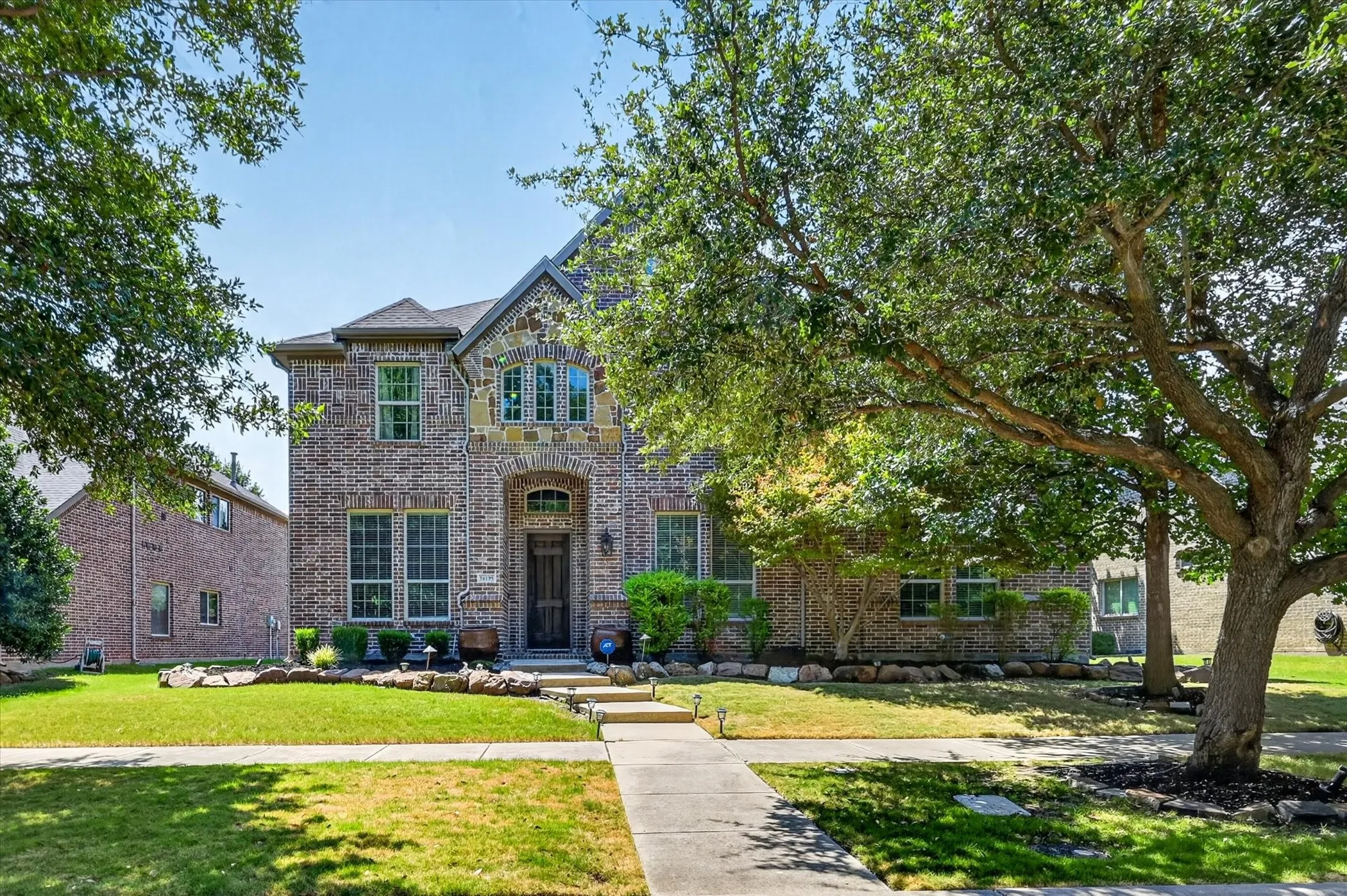 Brick and stone facade residence featuring an arched entry, multiple window styles, and a concrete walkway