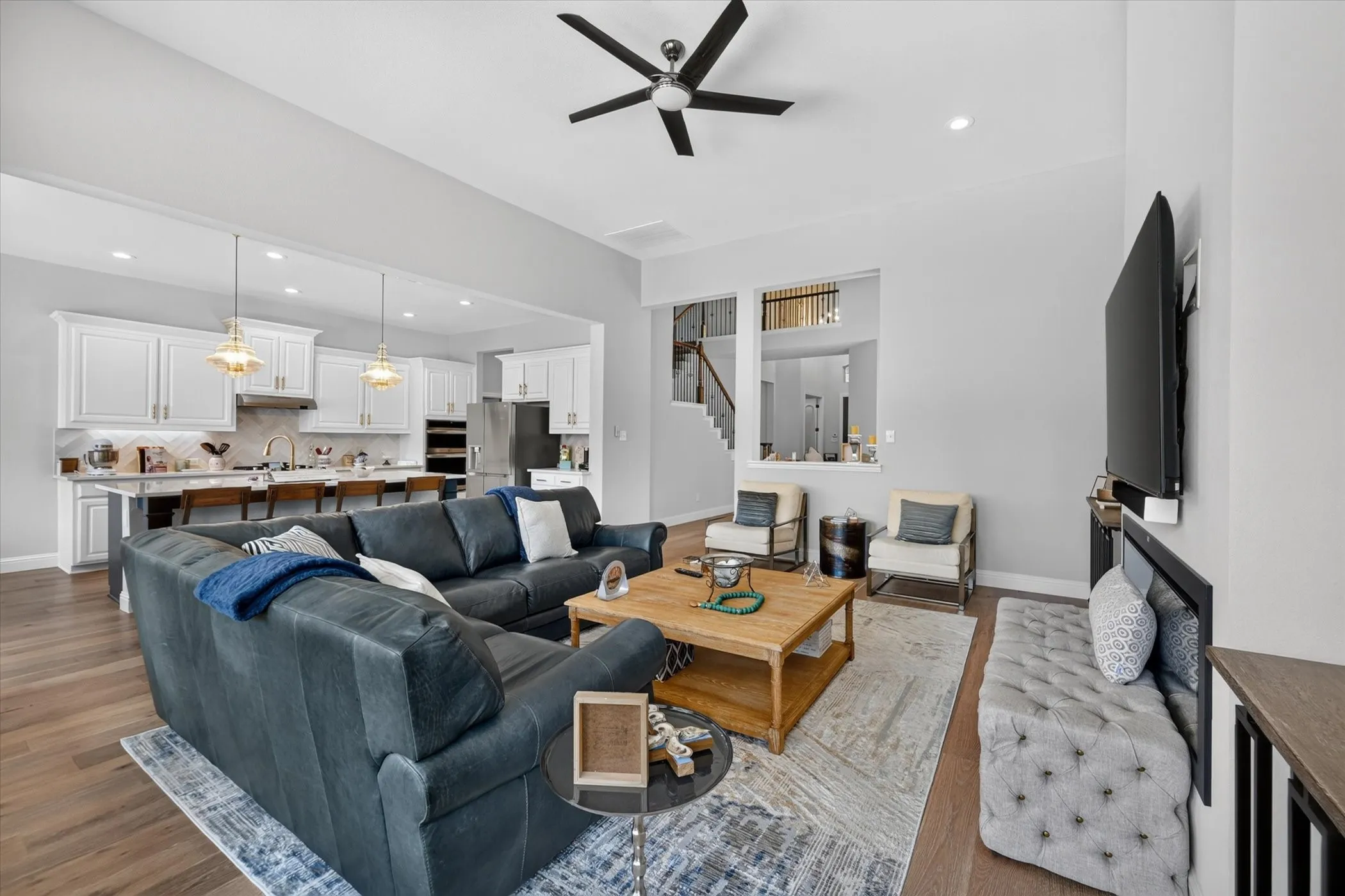 Open-concept living space with wood-finish flooring, a contemporary ceiling fan, recessed lighting, and a kitchen featuring white cabinetry, a large island, and stainless steel appliances