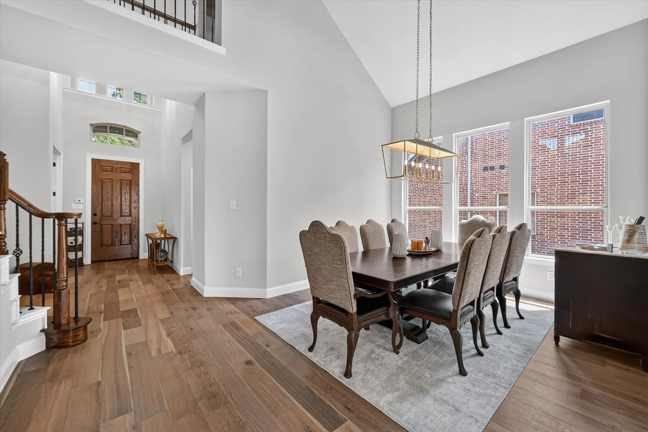 Vaulted ceilings, wood-finish flooring, staircase with wrought iron balusters, transom window, and a modern rectangular chandelier