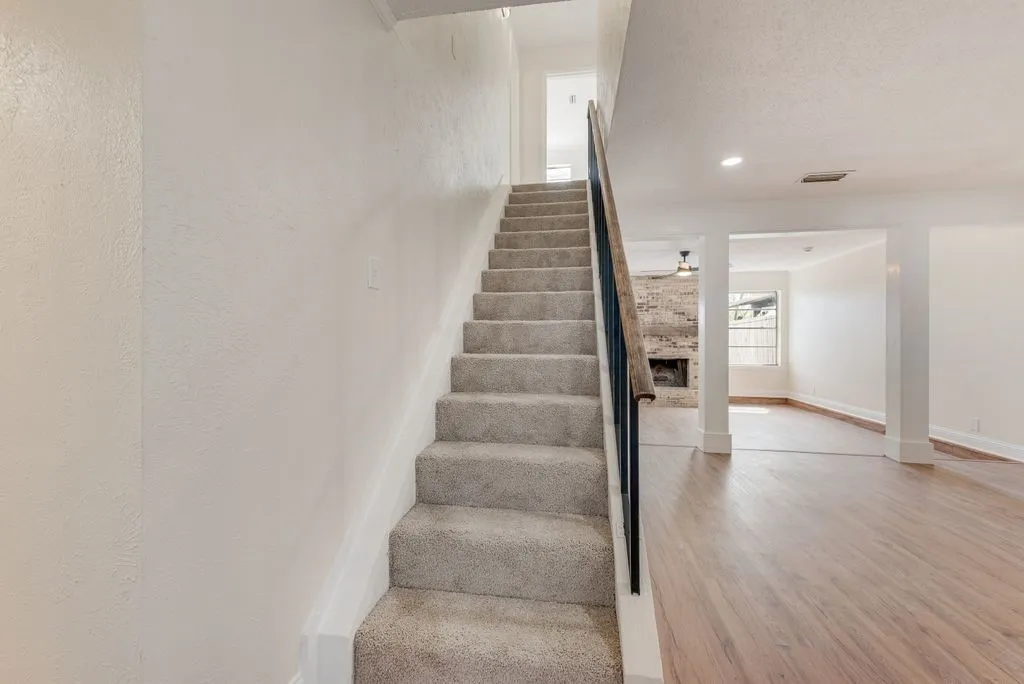 Carpeted staircase with an iron railing, wood-finish flooring, and a brick-finish fireplace