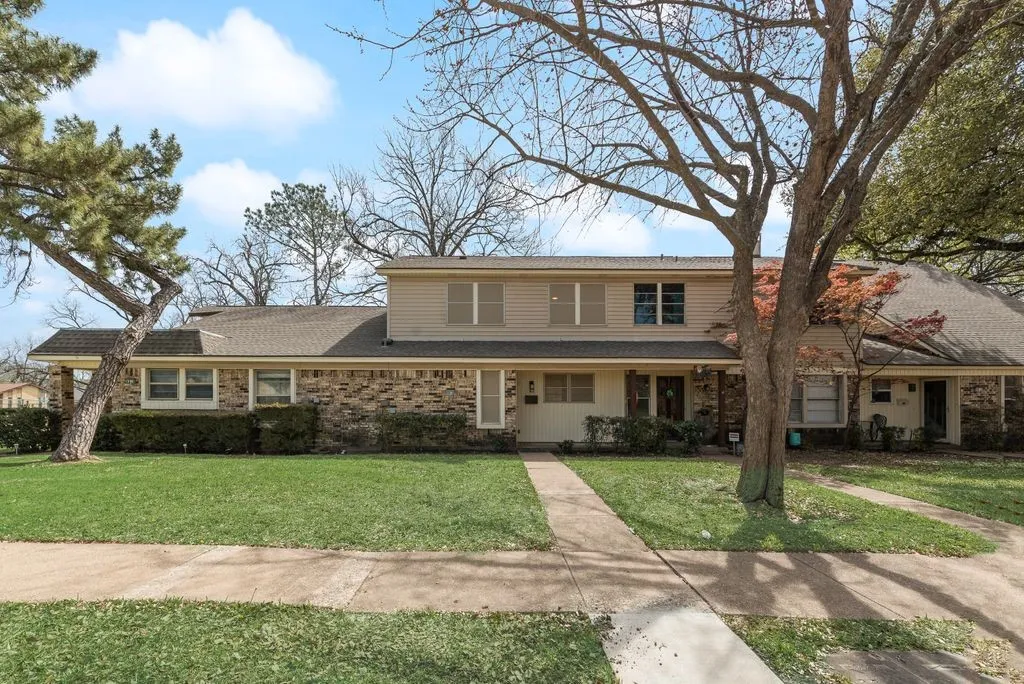 Brick and siding exterior with a covered front porch, dual driveways, a concrete walkway, and a manicured lawn
