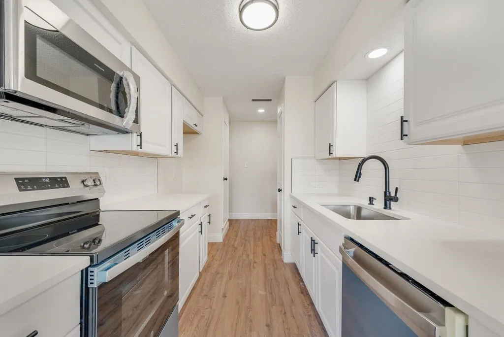 Galley kitchen featuring white cabinetry, stainless steel appliances, a matte black faucet, wood-finish flooring, and white countertops