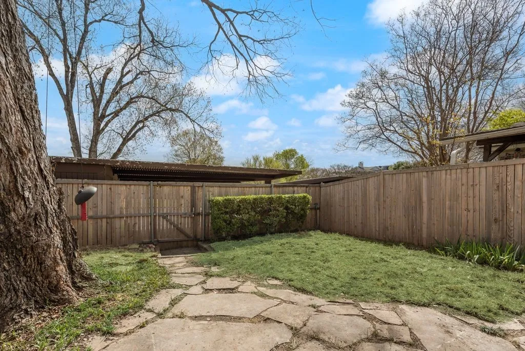 Landscaped backyard featuring a stone pathway, privacy fencing, mature trees, and a grassy area