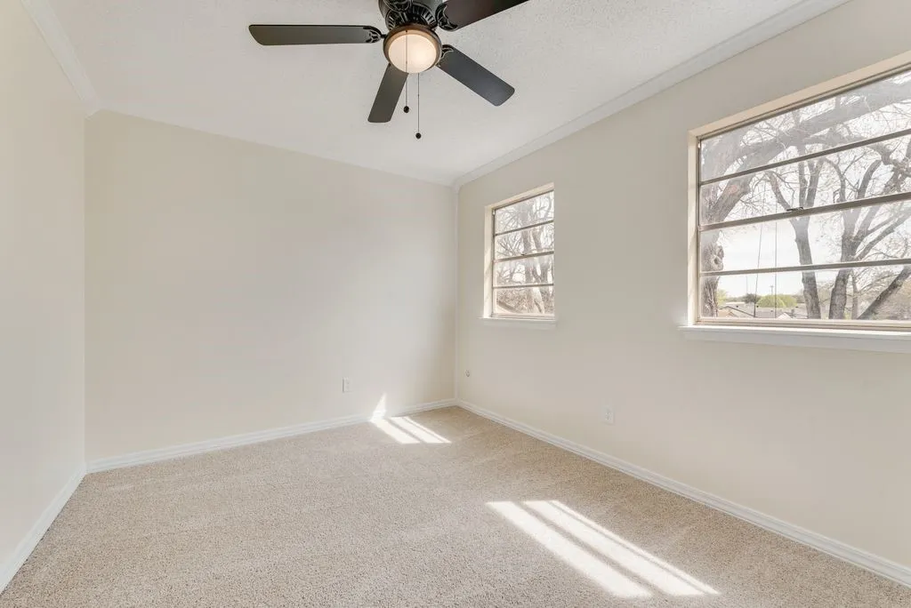 Neutral wall paint, crown molding, two windows with exterior views, and a ceiling fan with integrated lighting