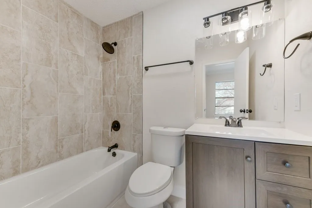 Shower/tub combination with ceramic tile surround, integrated vanity with white countertop, and contemporary lighting fixture
