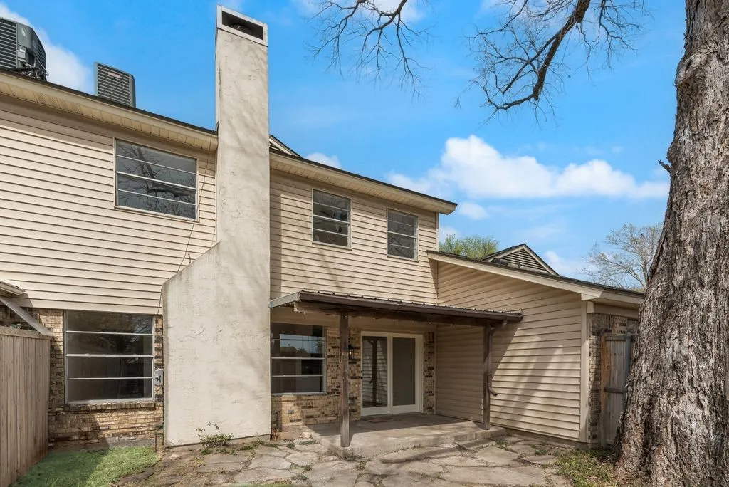 Rear exterior featuring horizontal siding, a stucco chimney, brick foundation, and a covered patio with stone flooring