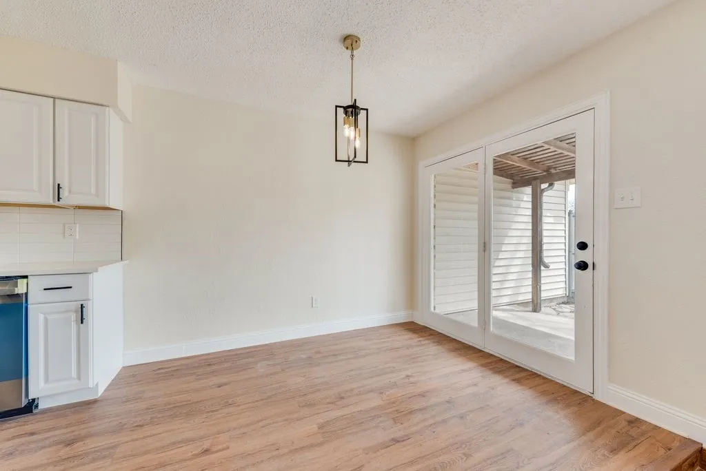 Wood-finish flooring, white cabinetry with black hardware, subway tile backsplash, contemporary pendant lighting, and a double glass-panel door
